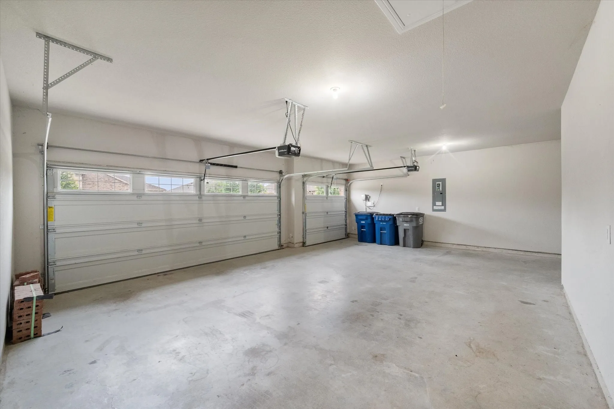 Spacious THREE-car garage with concrete flooring, two automatic garage doors, upper transom windows and overhead lighting