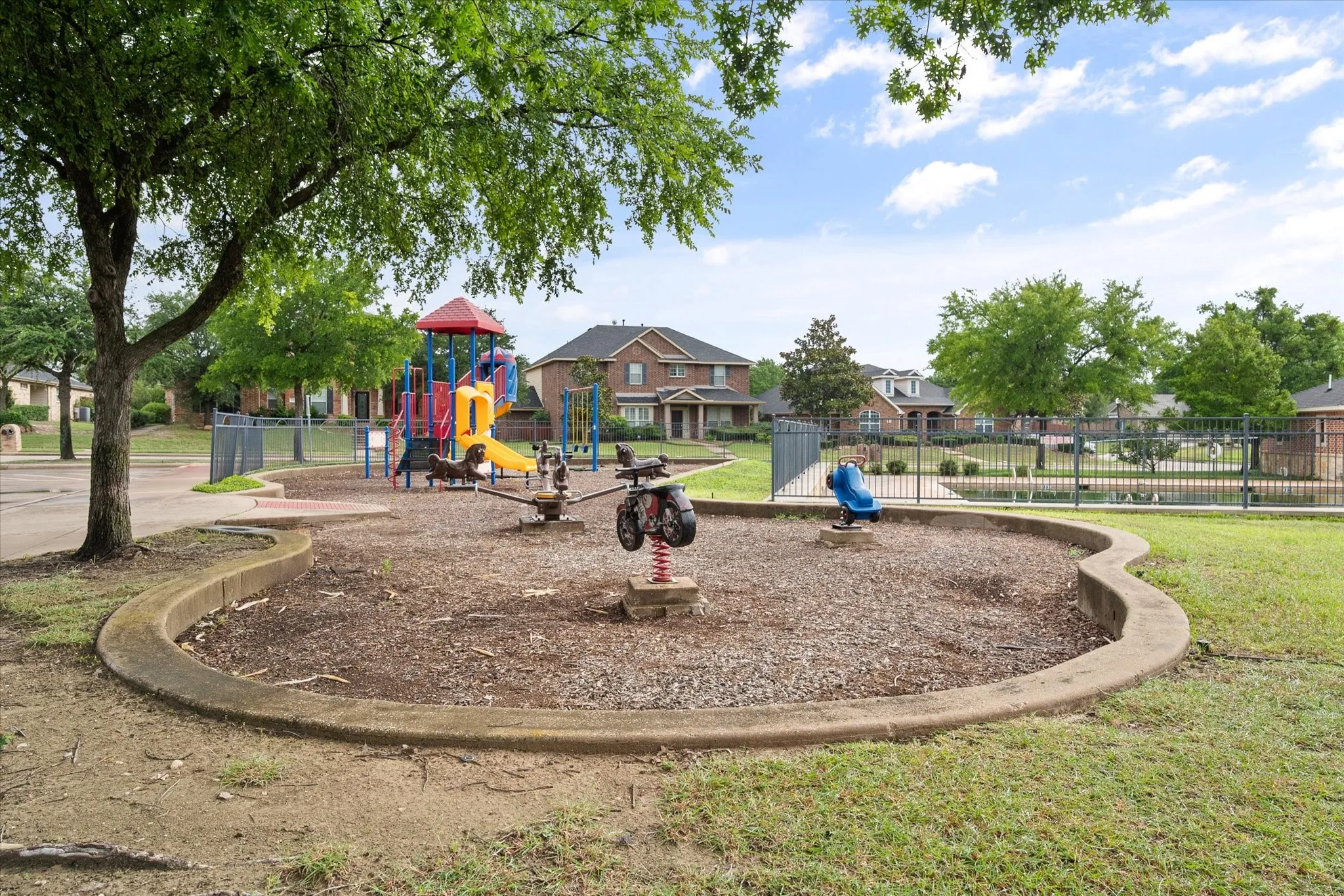 Community playground featuring a colorful play structure, spring riders, and a perimeter fence
