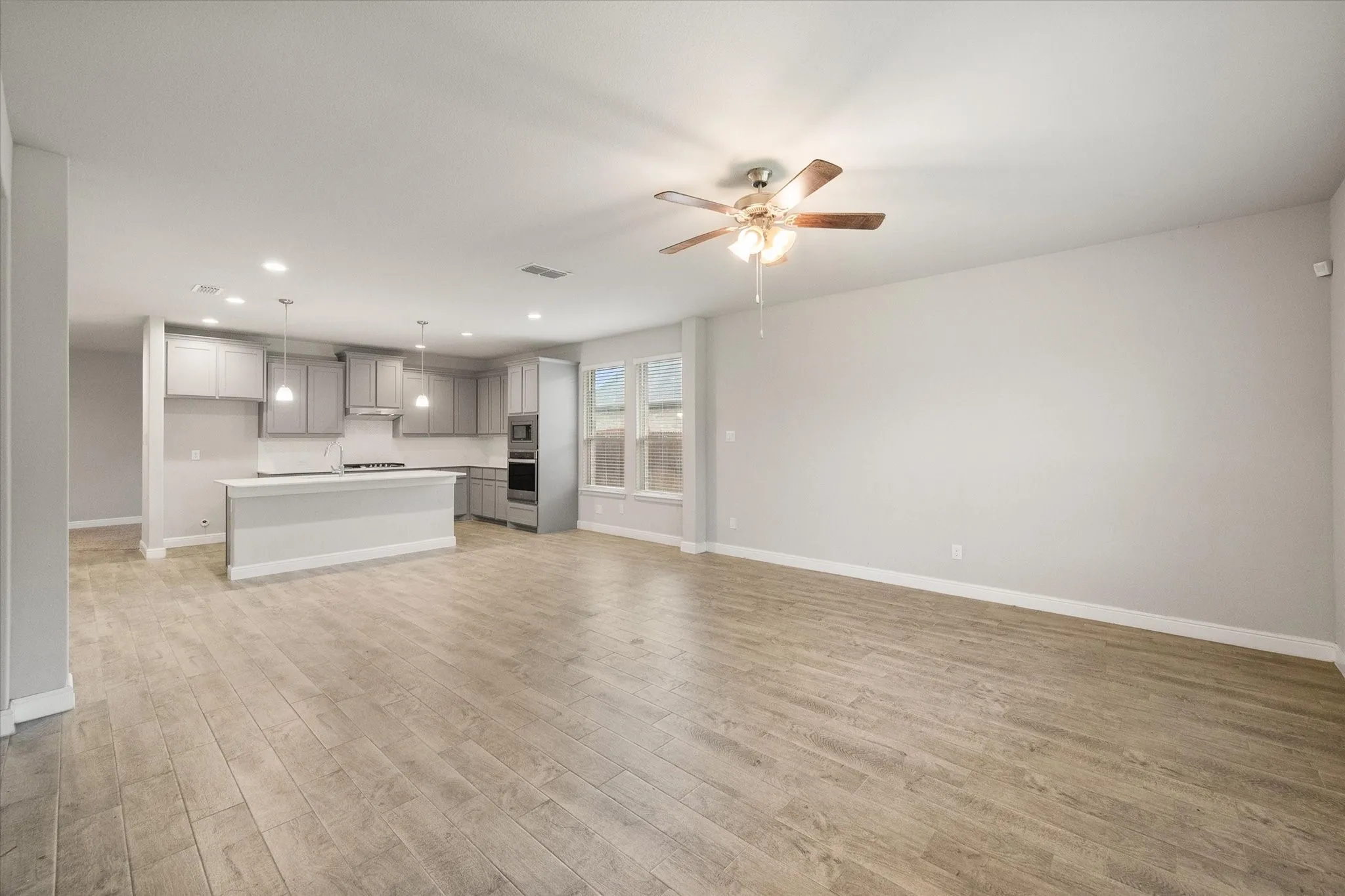 Spacious open-concept living area featuring wood-look tile flooring, ceiling fan, recessed lighting, and large windows providing ample illumination