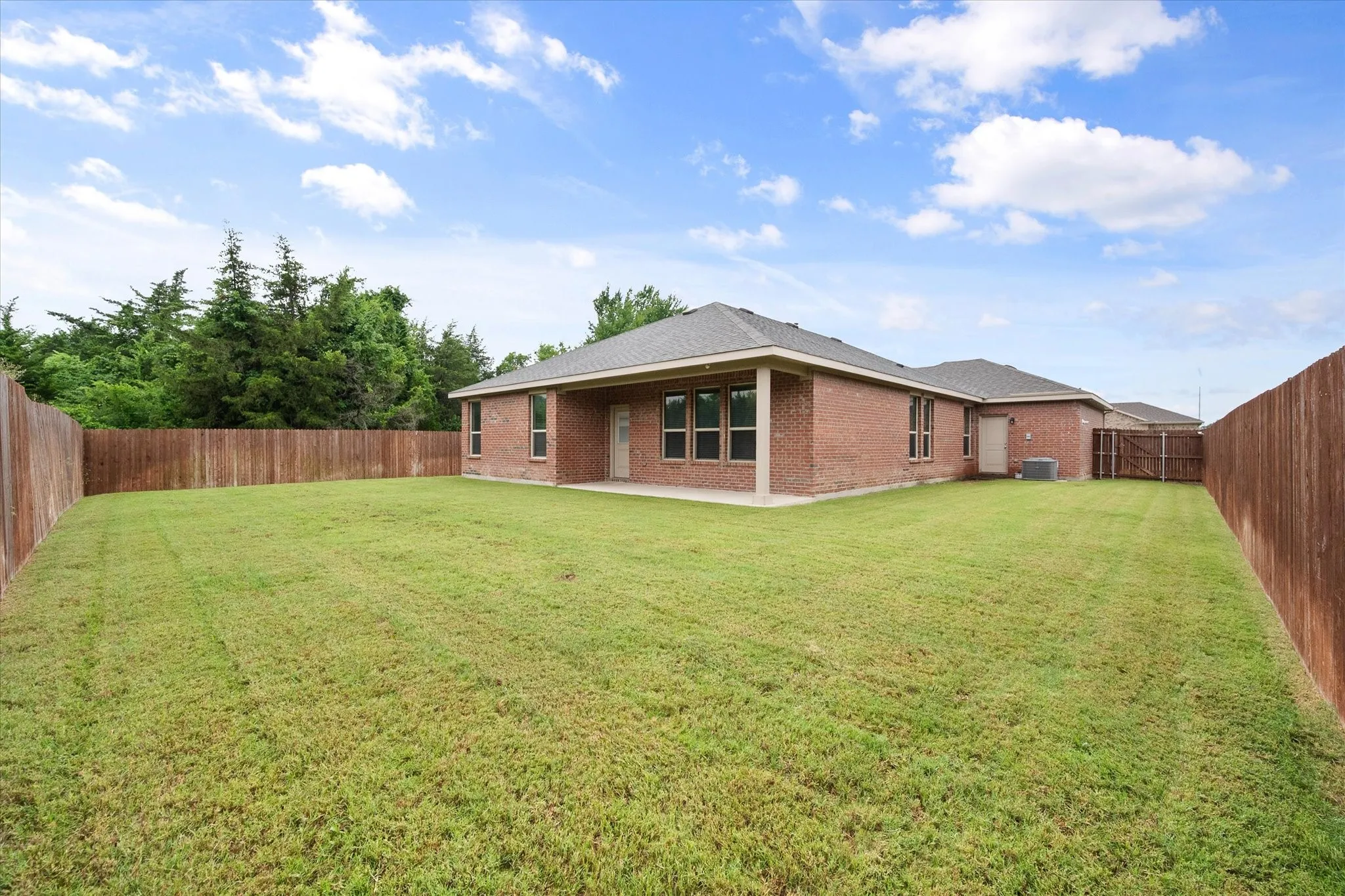 Expansive backyard featuring a manicured lawn, full privacy fencing, and a brick exterior with multiple windows. Treed greenbelt on one side and also behind this home!