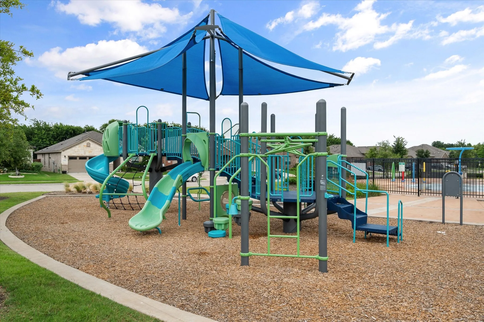 Community playground featuring multiple slides, climbing structures, and a protective shade canopy over a wood chip surface
