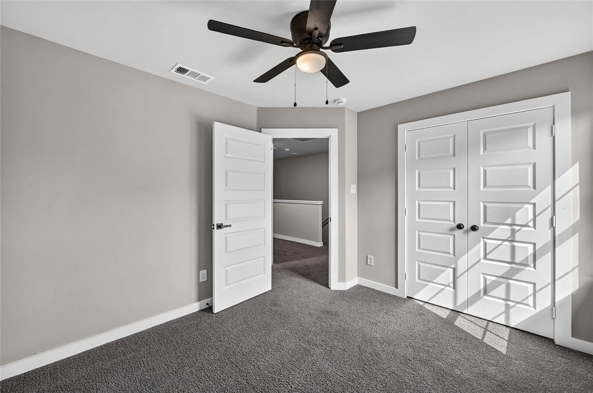 Light gray wall paint, dark gray carpeting, paneled interior doors, ceiling fan with integrated lighting, and white trim throughout