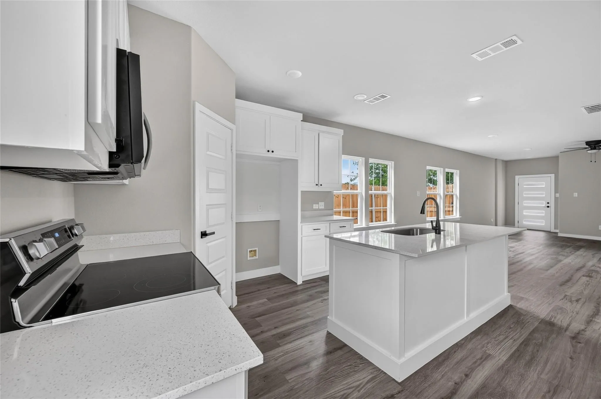 Kitchen featuring white cabinetry, light-toned countertops, a center island with sink and faucet, and wood-finish flooring