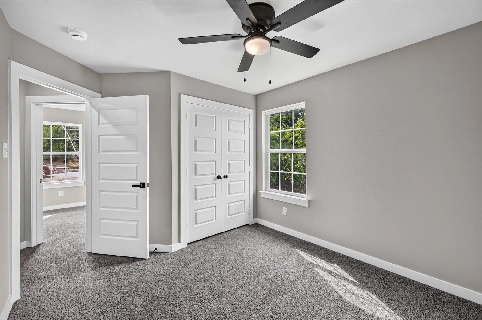 Neutral wall paint, carpet flooring, ceiling fan with integrated lighting, paneled doors with matte black hardware, and double-hung windows