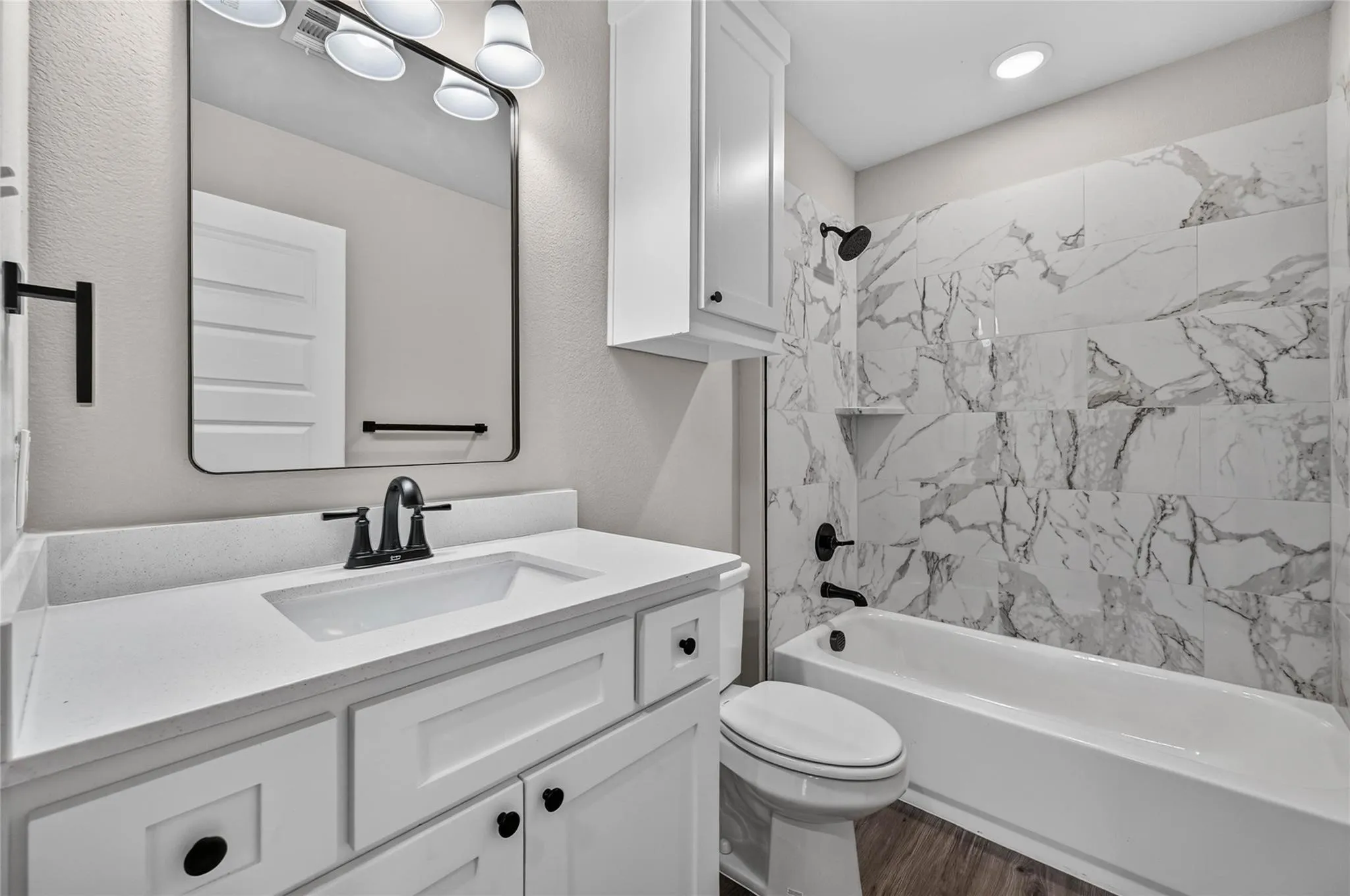 White vanity with an integrated sink and matte black faucet, framed mirror, and a white bathtub with a tile surround featuring a built-in niche