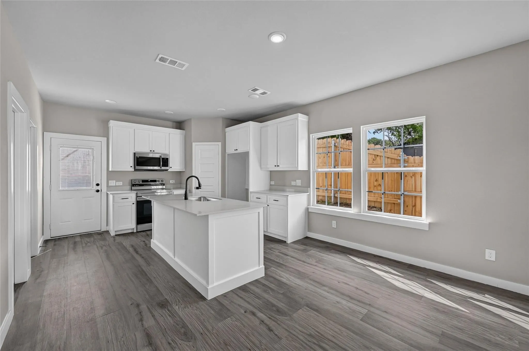 Open-concept kitchen featuring an island with sink, white shaker cabinetry, stainless steel appliances, and wood-finish flooring