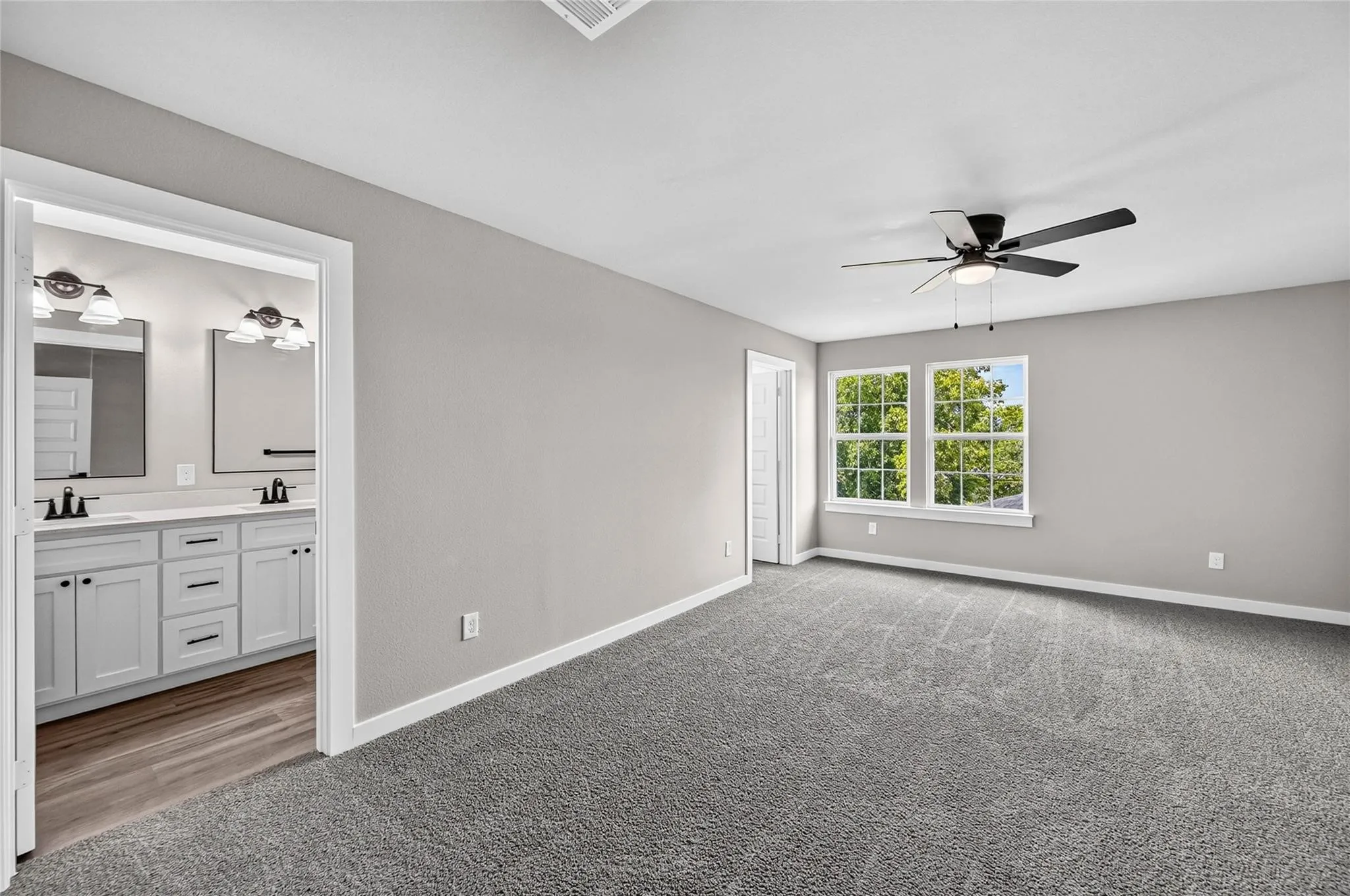 Spacious room featuring neutral carpeting, a ceiling fan with integrated lighting, and two large windows