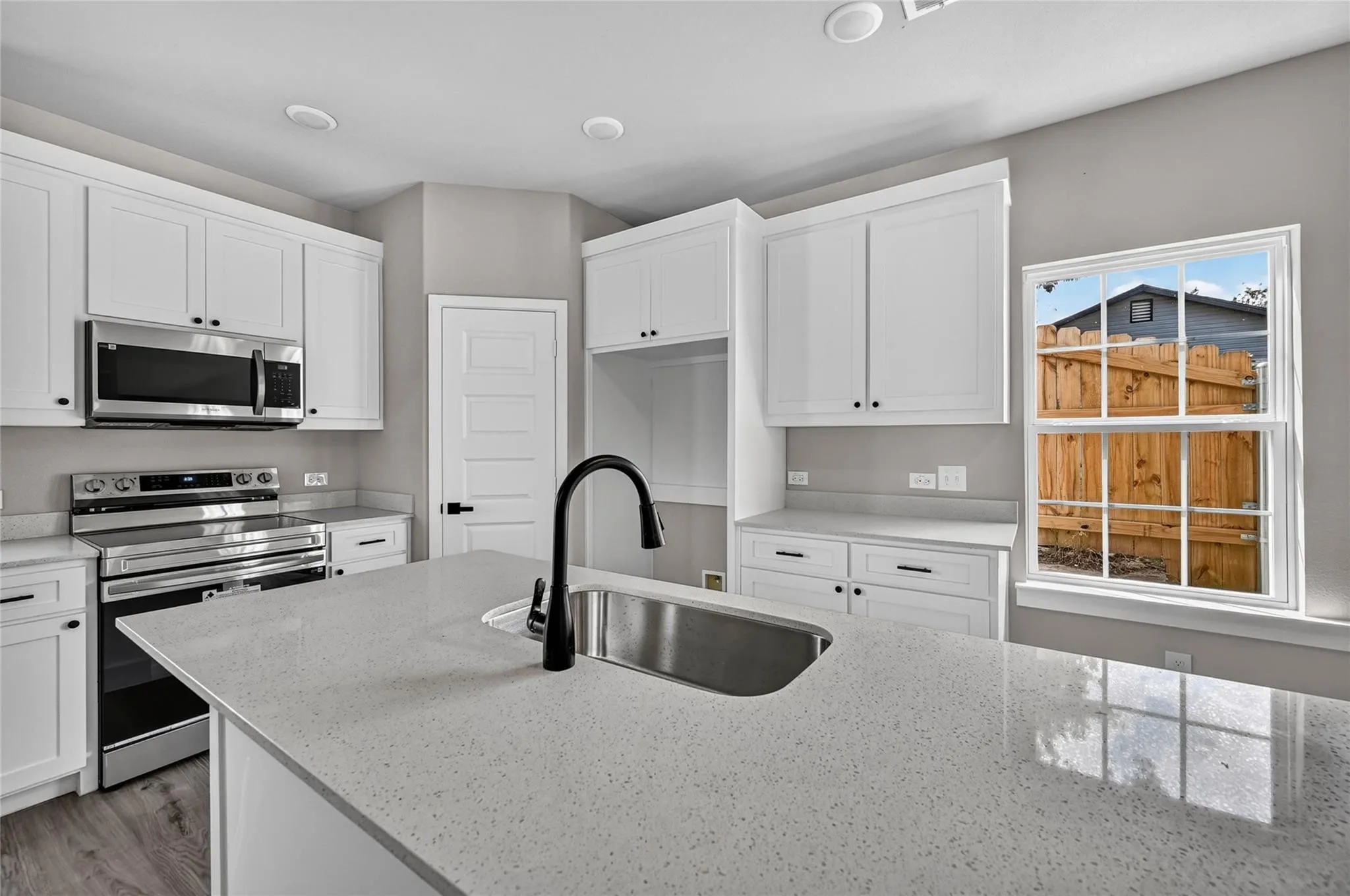 White shaker-style cabinetry, stainless steel appliances, light-colored countertops, wood-finish flooring, and a single-basin sink with a matte black faucet