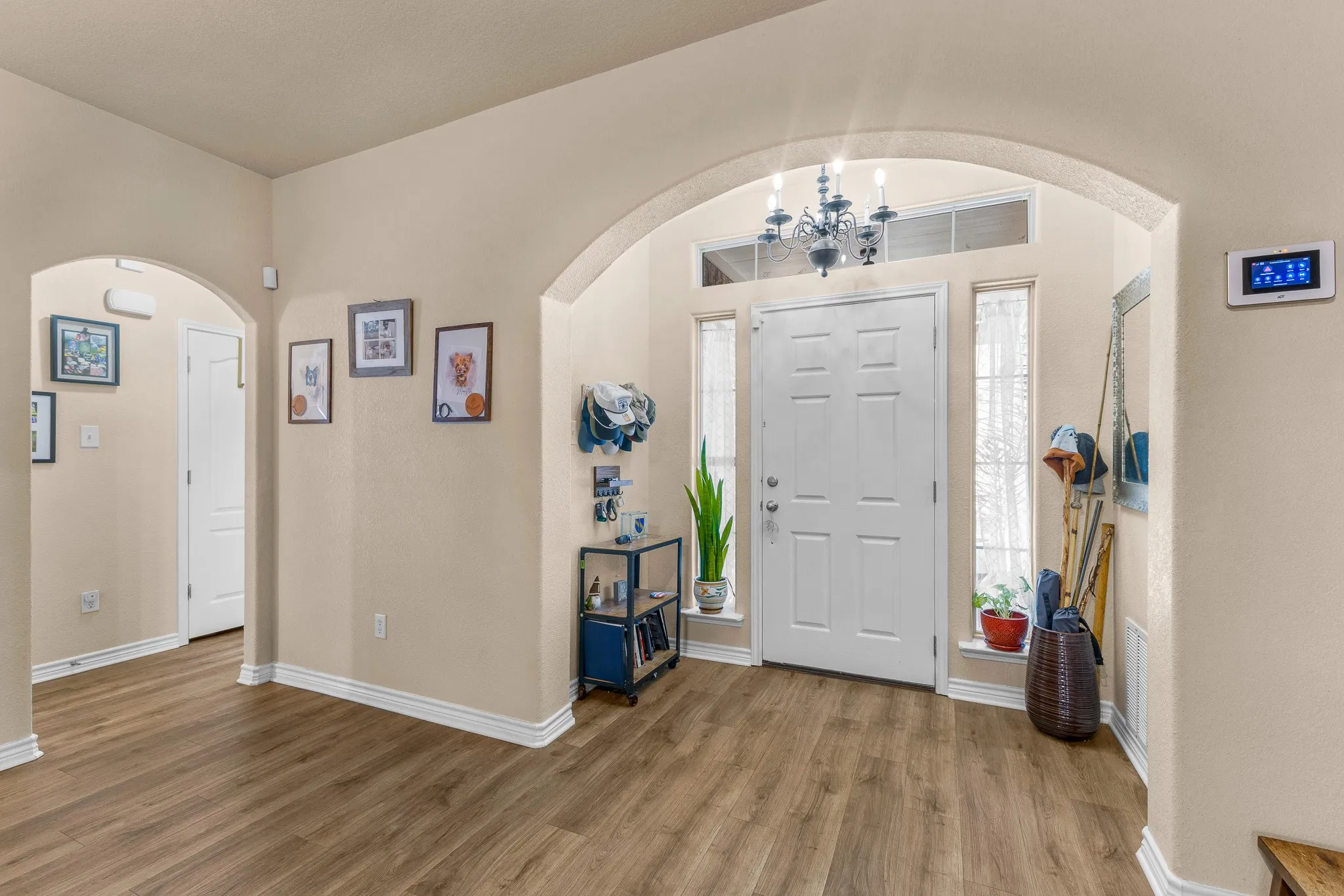 Entryway featuring wood-finish flooring, an arched doorway, a white paneled door with sidelights, and a chandelier
