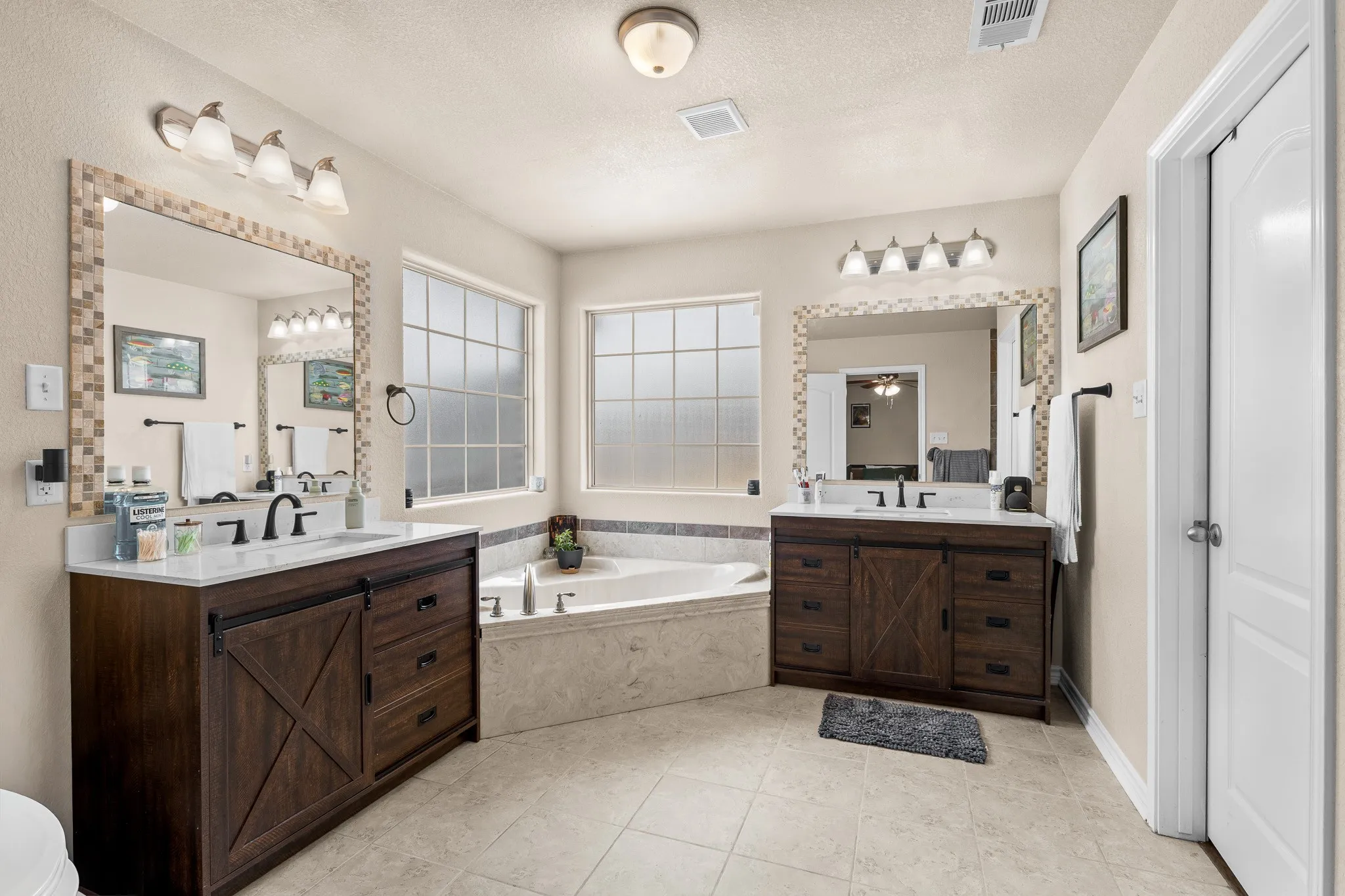 Dual wood-finish vanities with countertop sinks, a built-in corner bathtub, and multiple frosted glass windows