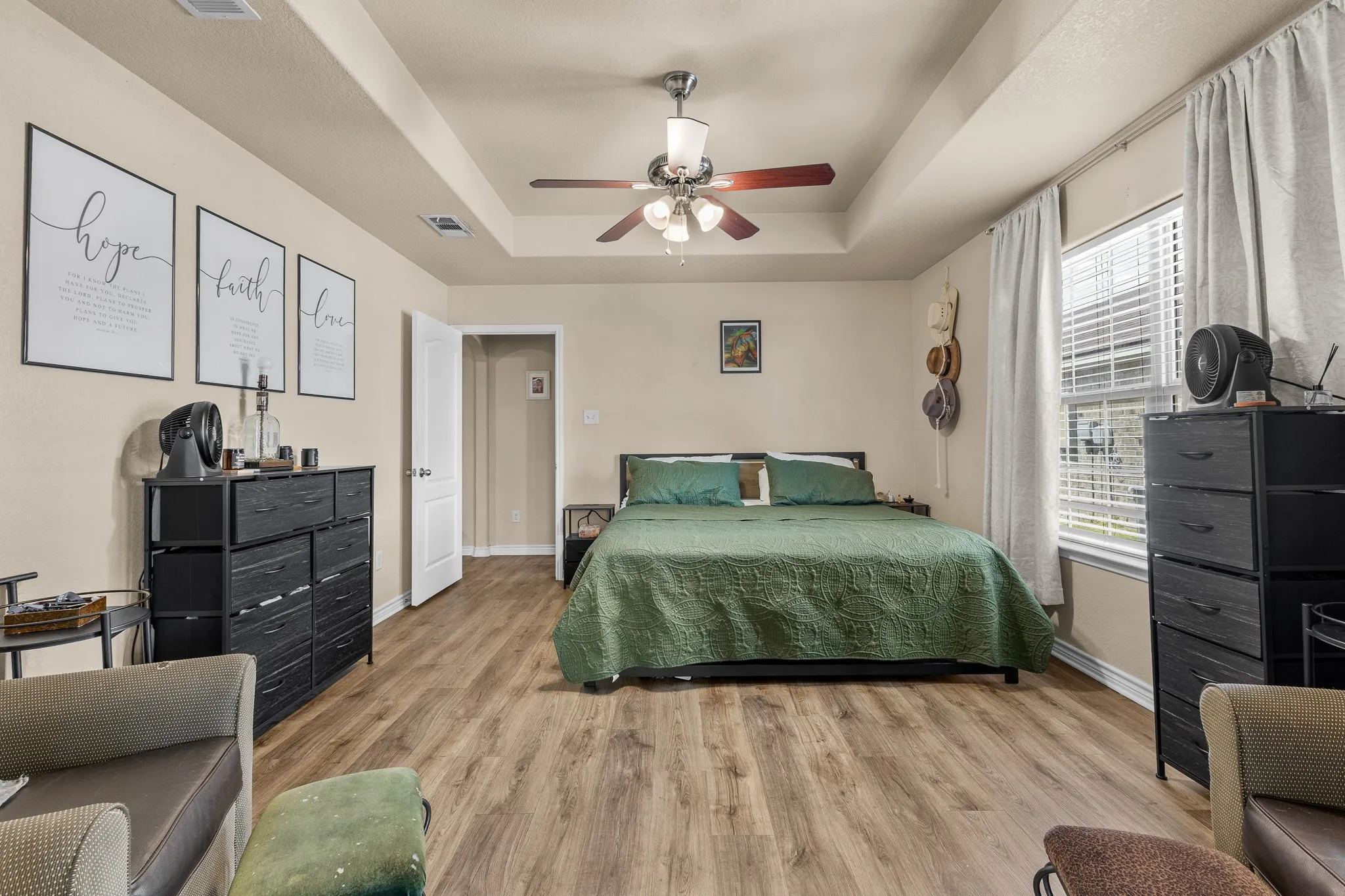 Tray ceiling with a ceiling fan light fixture, wood-finish flooring, and window with blinds