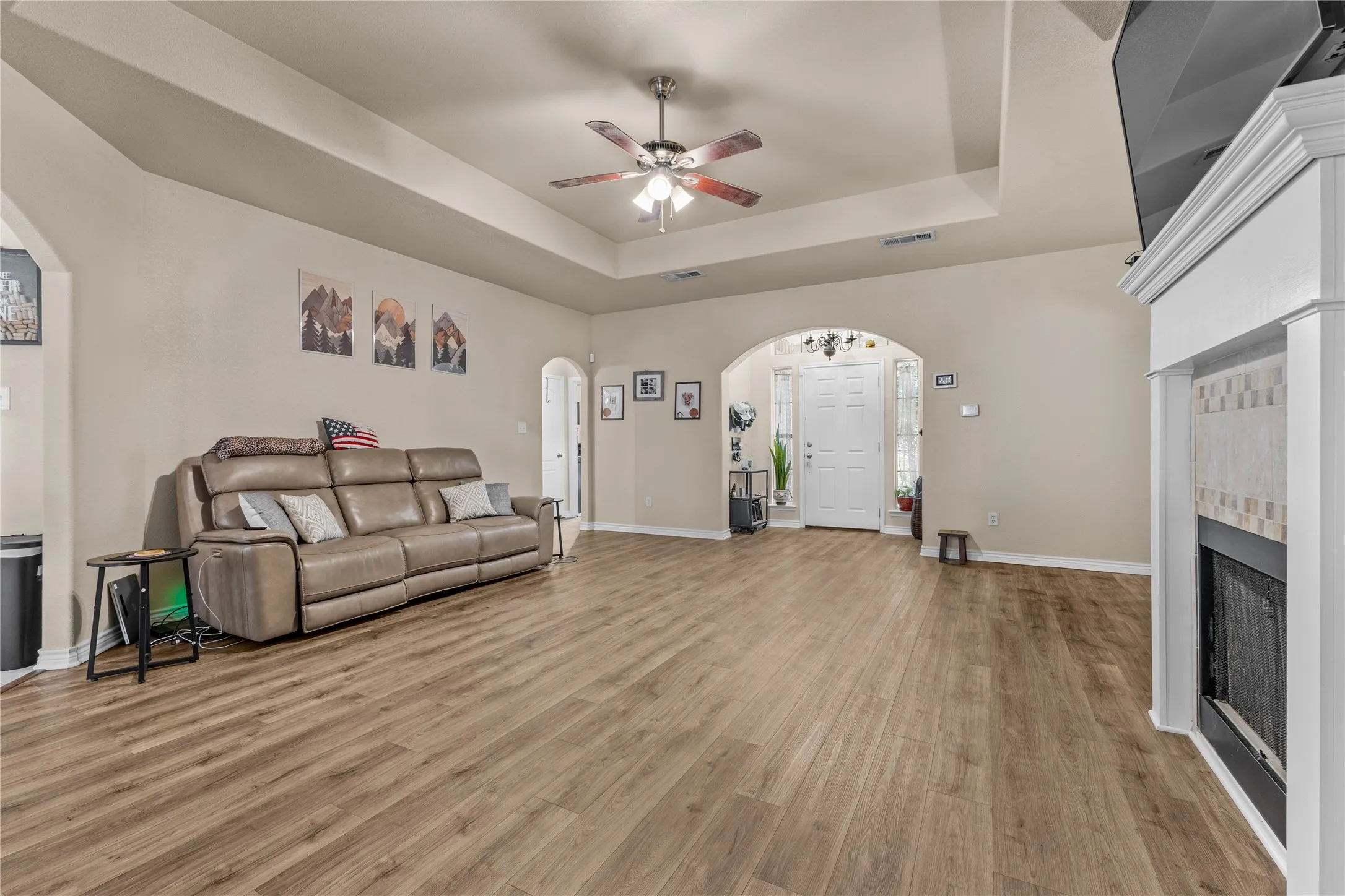 Spacious living area featuring wood-finish flooring, a tray ceiling, and a ceiling fan
