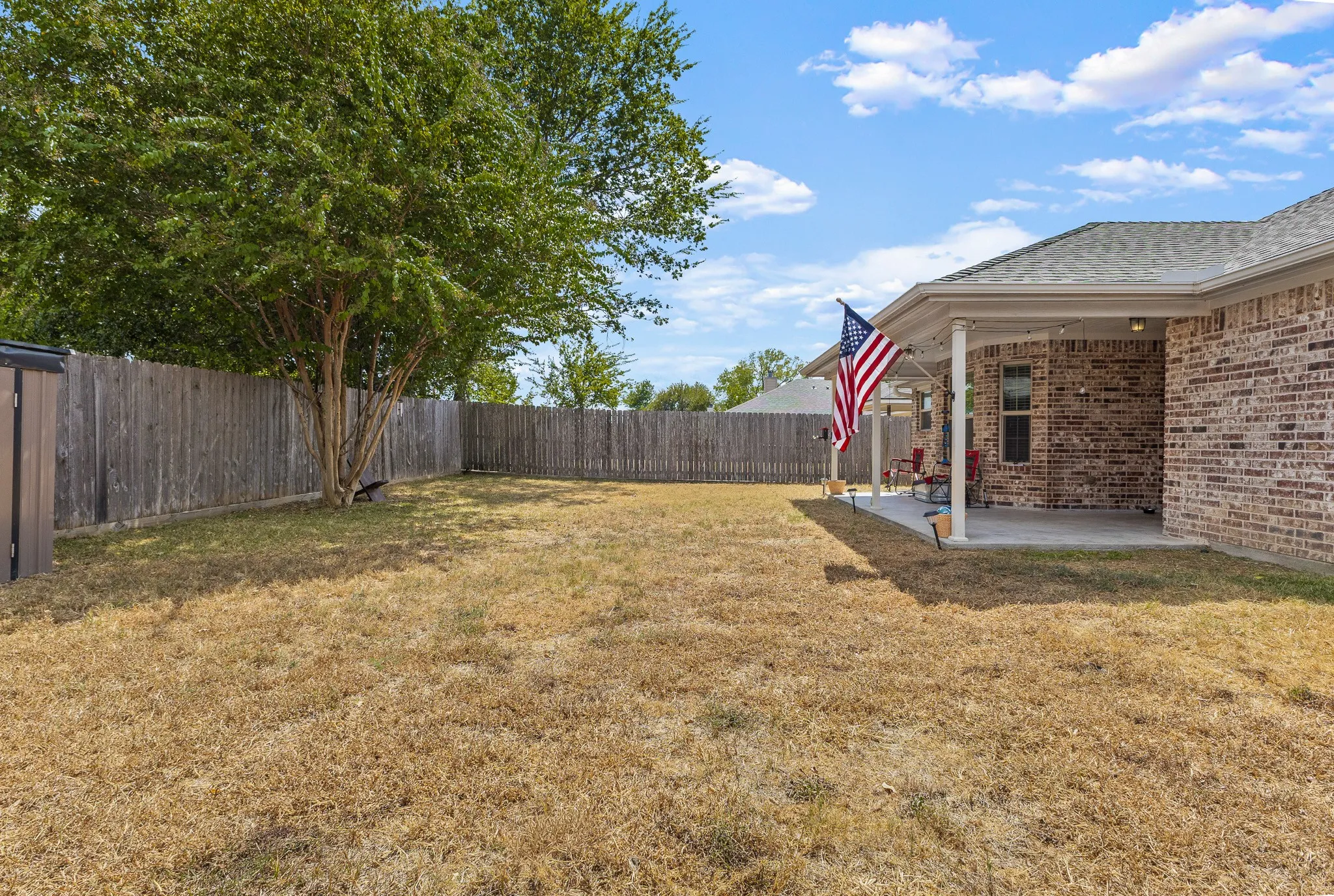 Expansive backyard featuring a mature tree, wood privacy fencing, and a covered concrete patio
