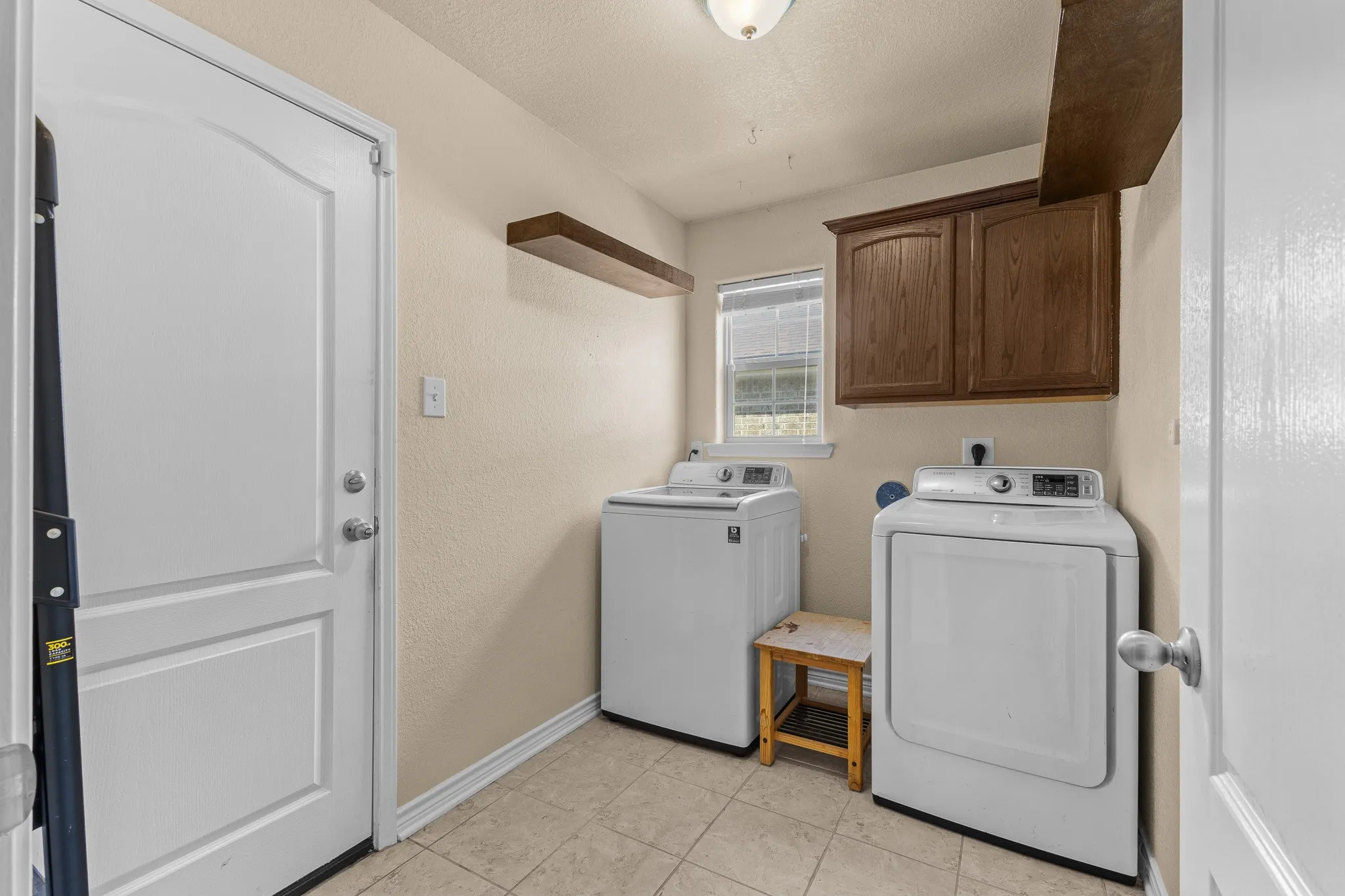 Utility room with tile flooring, wood-finish cabinetry, and a window for natural light