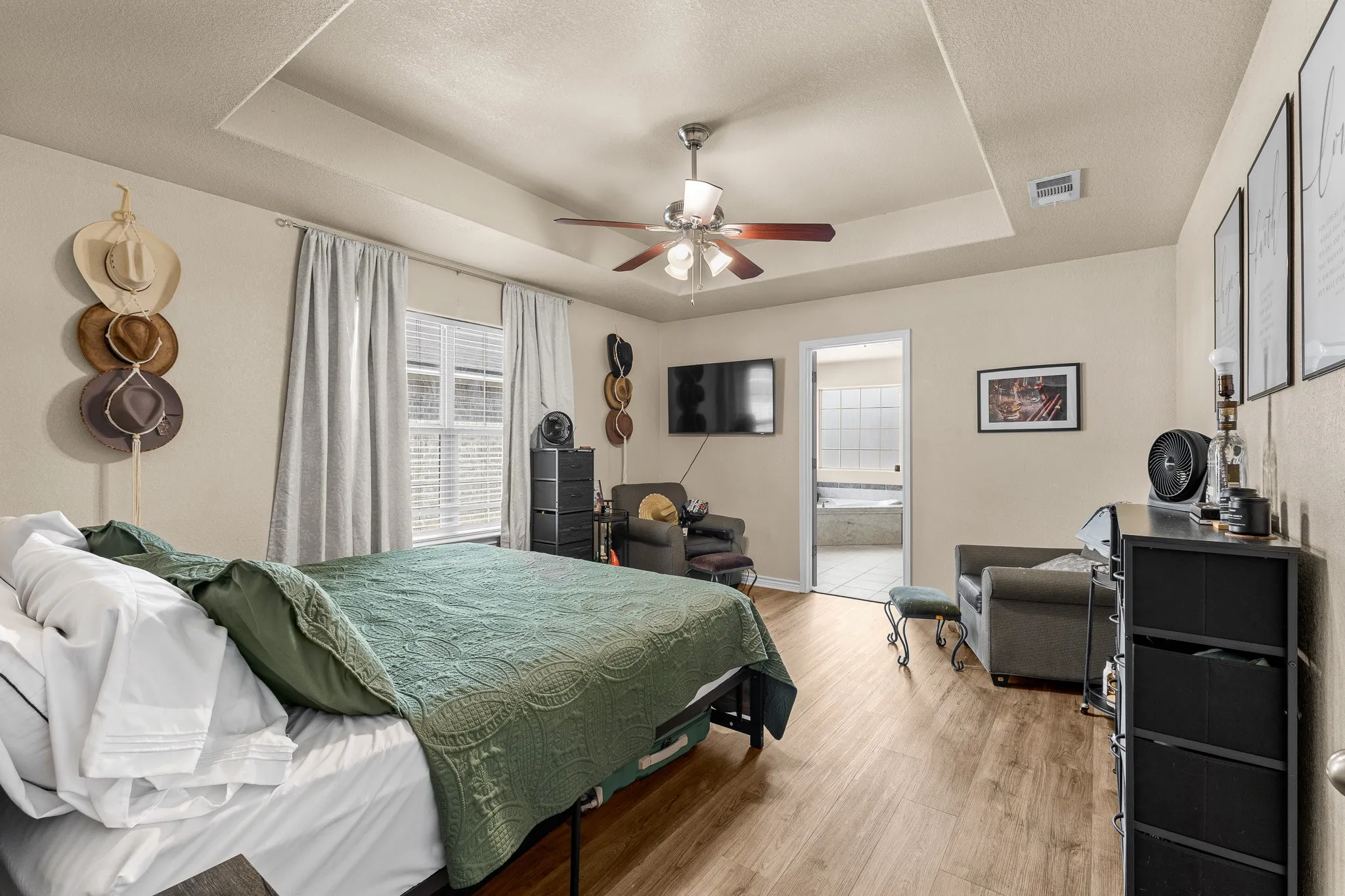 Tray ceiling with a ceiling fan, wood-finish flooring, and a large window with blinds