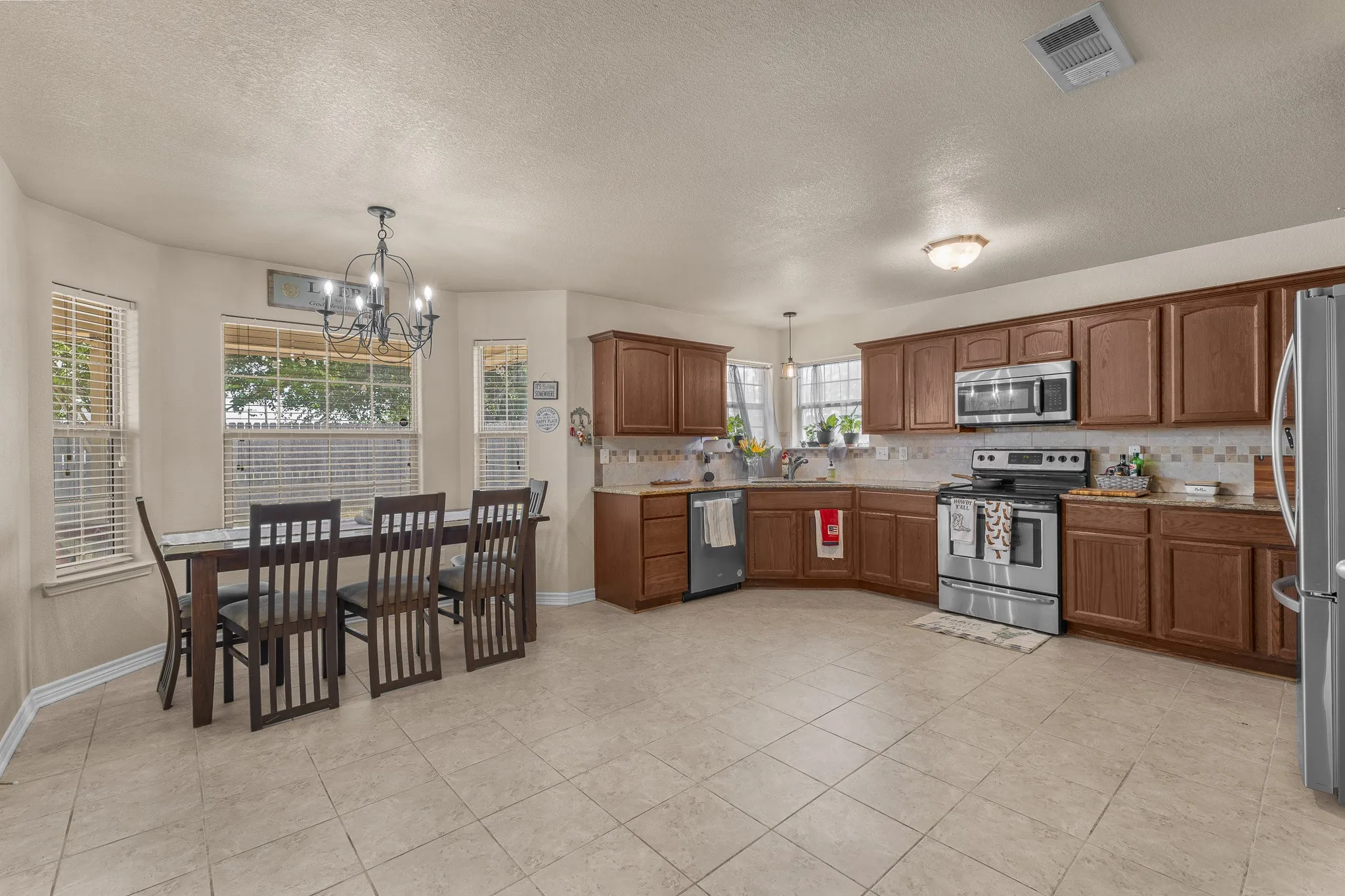 Kitchen and dining area featuring tile flooring, wood cabinetry, stainless steel appliances, and multiple windows