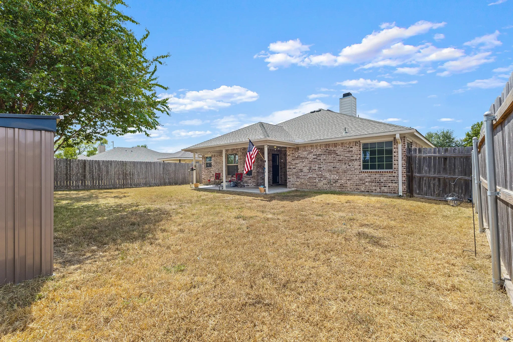 Expansive backyard featuring a privacy fence, brick exterior, covered patio, and storage shed