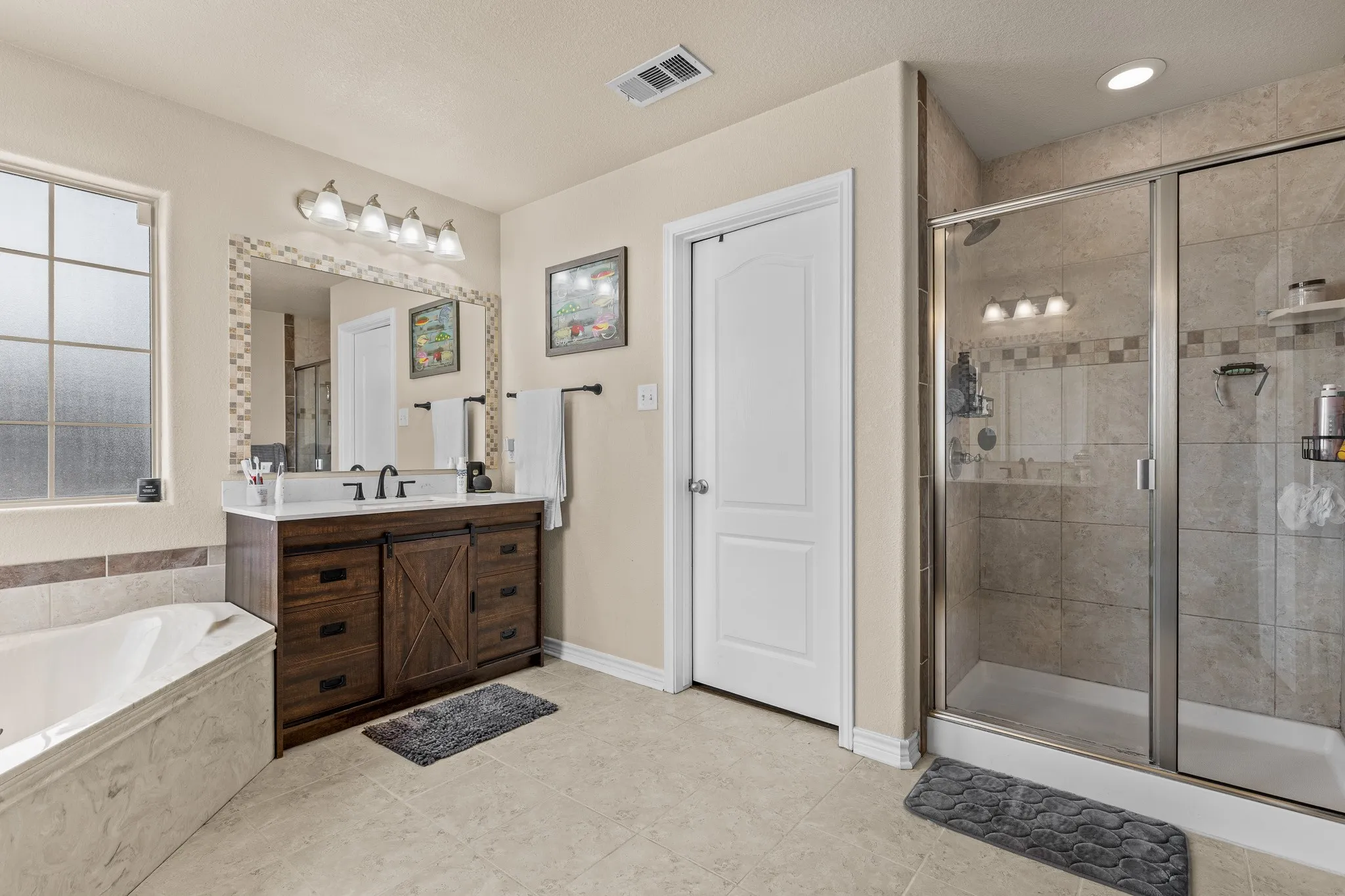 Walk-in shower with glass enclosure, wood-finish vanity with countertop sink, built-in bathtub, tiled flooring, and mosaic-tiled mirror