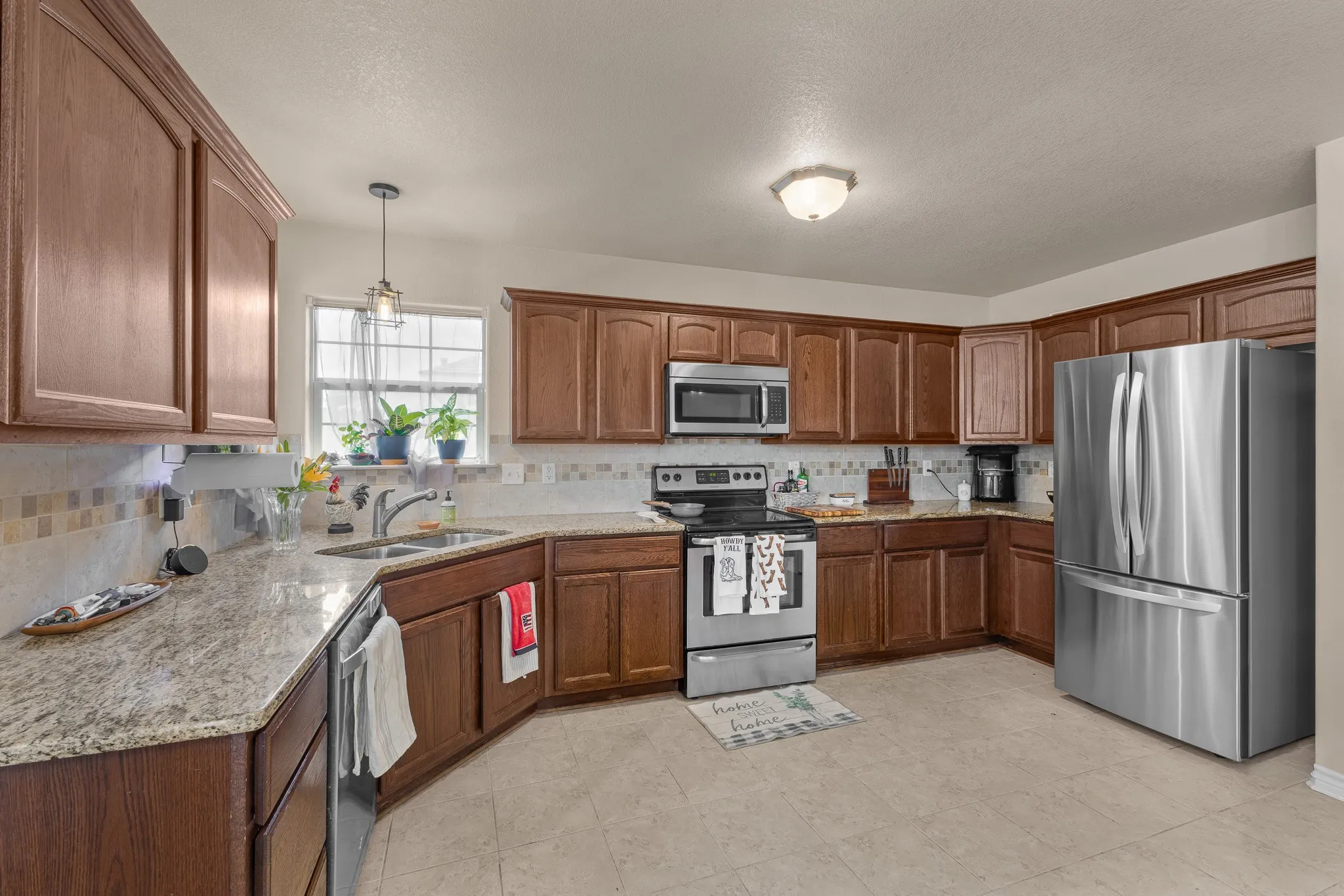 Kitchen featuring wood cabinetry, light-toned countertops, a mosaic tile backsplash, stainless steel appliances, and a window above the sink
