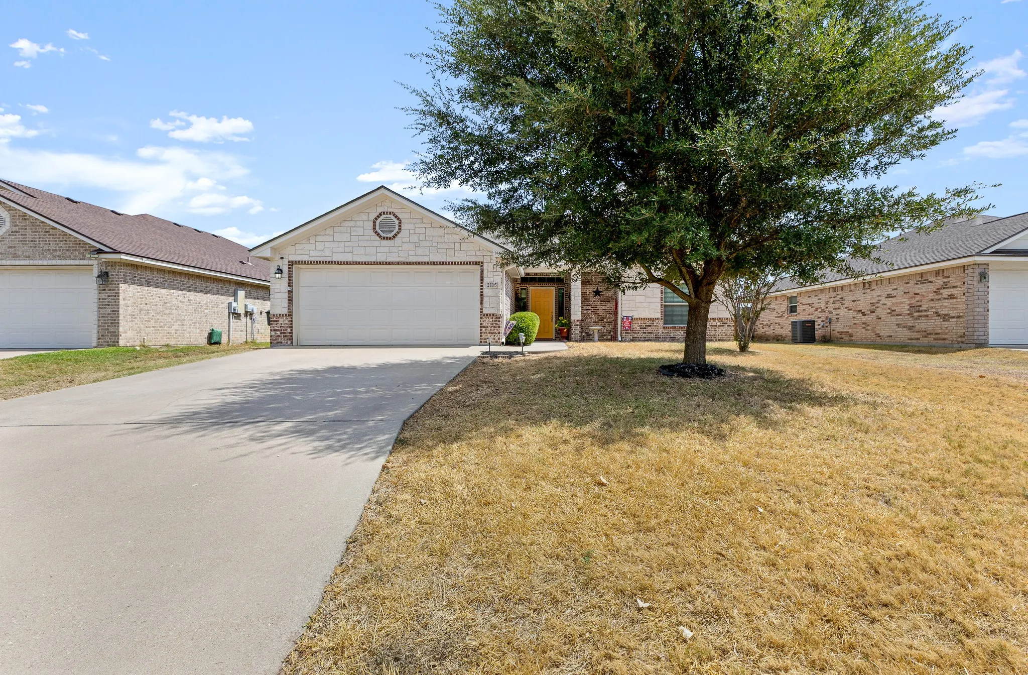 Brick and stone facade, attached garage, concrete driveway, and mature tree