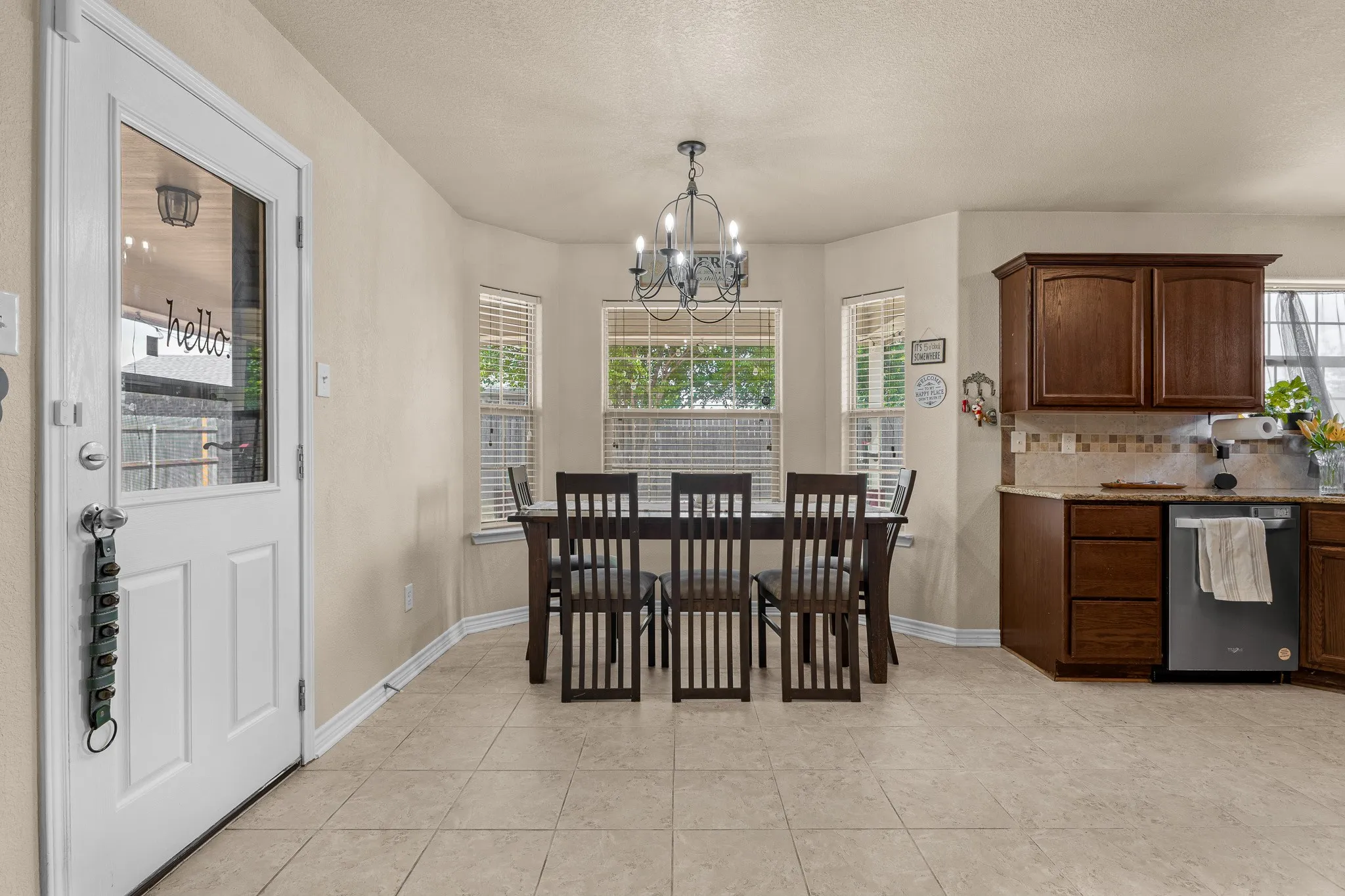 Tiled flooring throughout, kitchen with wood-finish cabinetry, and a bay window dining area with a chandelier