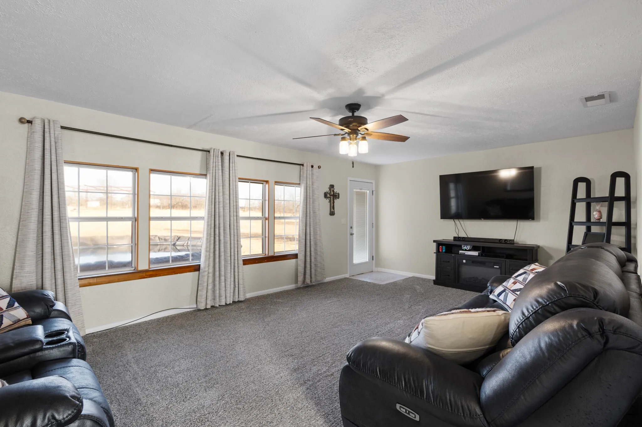 Neutral wall paint, ceiling fan with integrated lighting, multiple windows, carpet flooring, and a glass-paneled door
