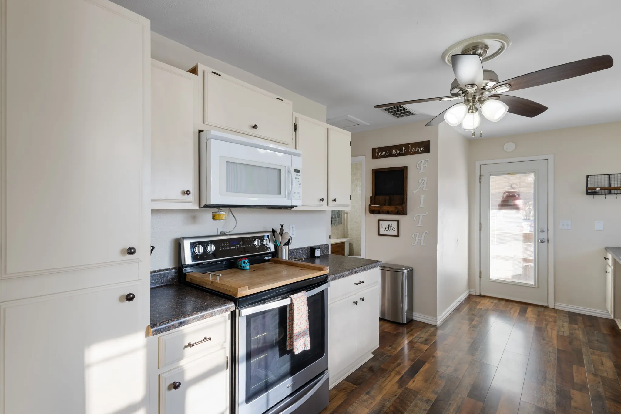 White cabinetry with dark hardware, undermount microwave, black electric range, dark speckled countertops, and wood-finish flooring