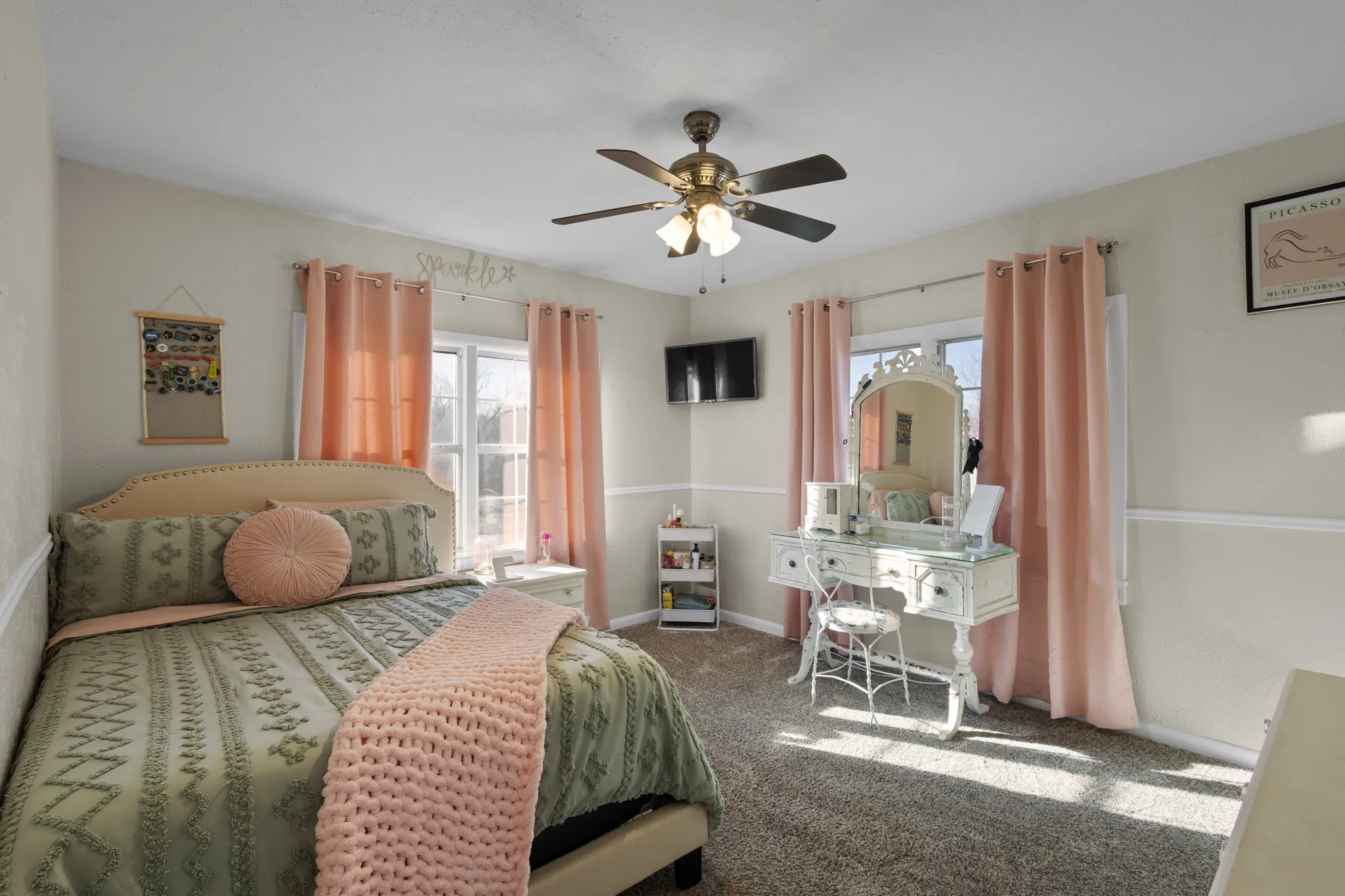 Carpeted bedroom featuring a ceiling fan, two large windows, and chair rail molding