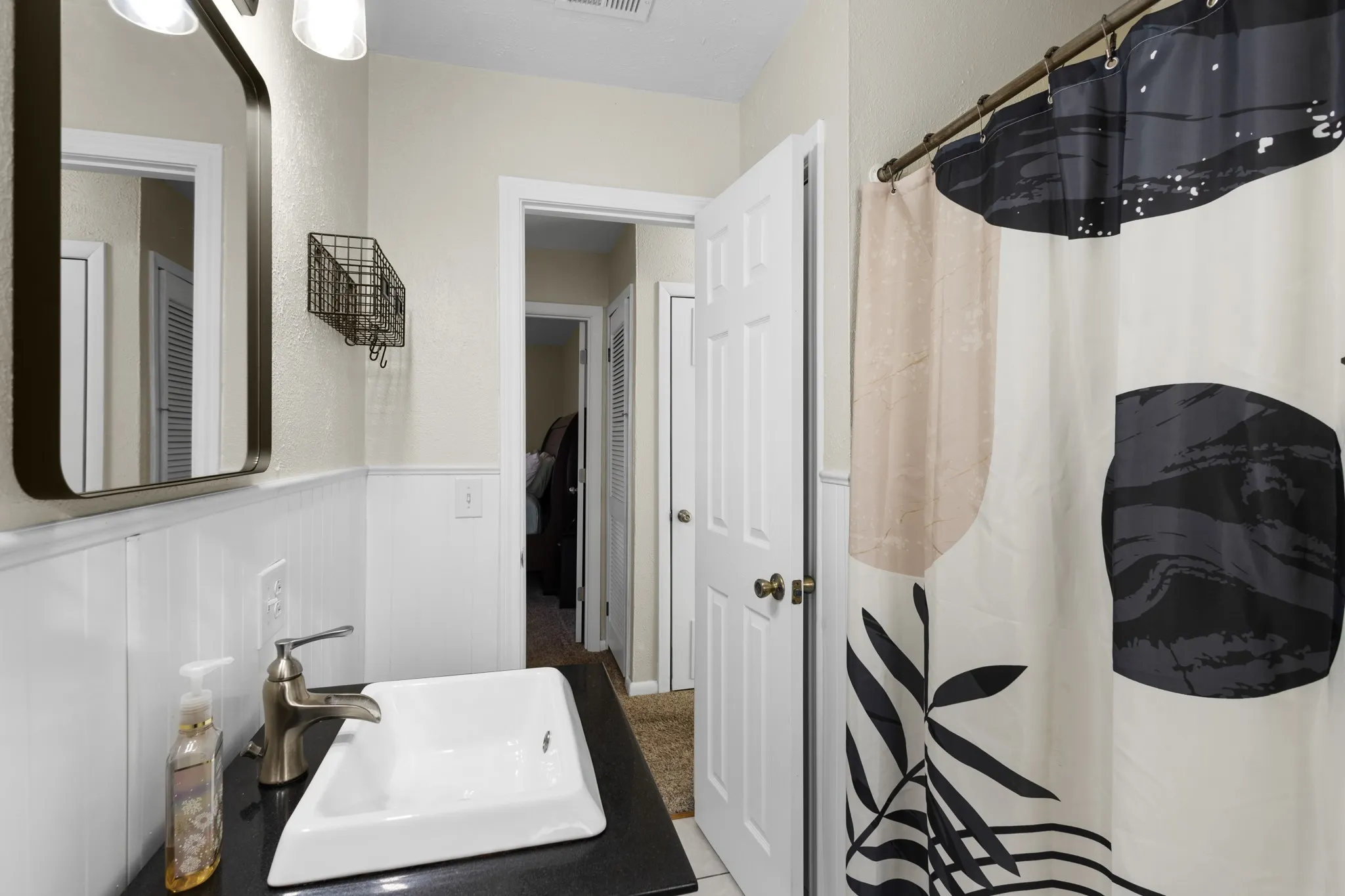 White wainscoting, a vessel sink with a brushed nickel faucet, a dark countertop, and a framed vanity mirror