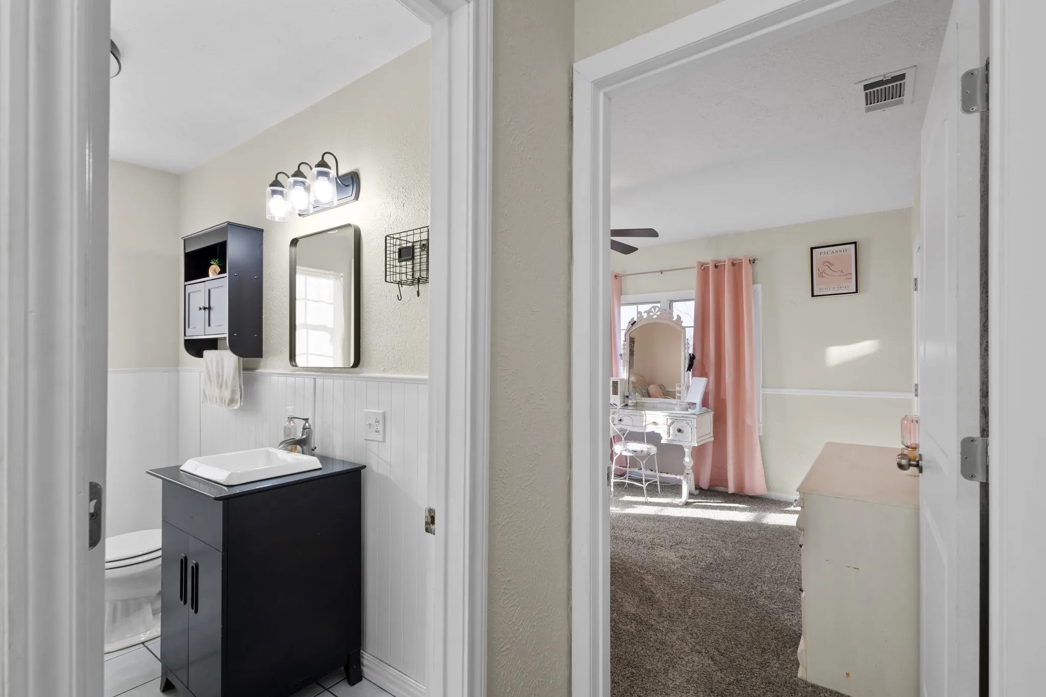 Bathroom with black vanity, vessel sink, wall-mounted storage, and wainscoting
