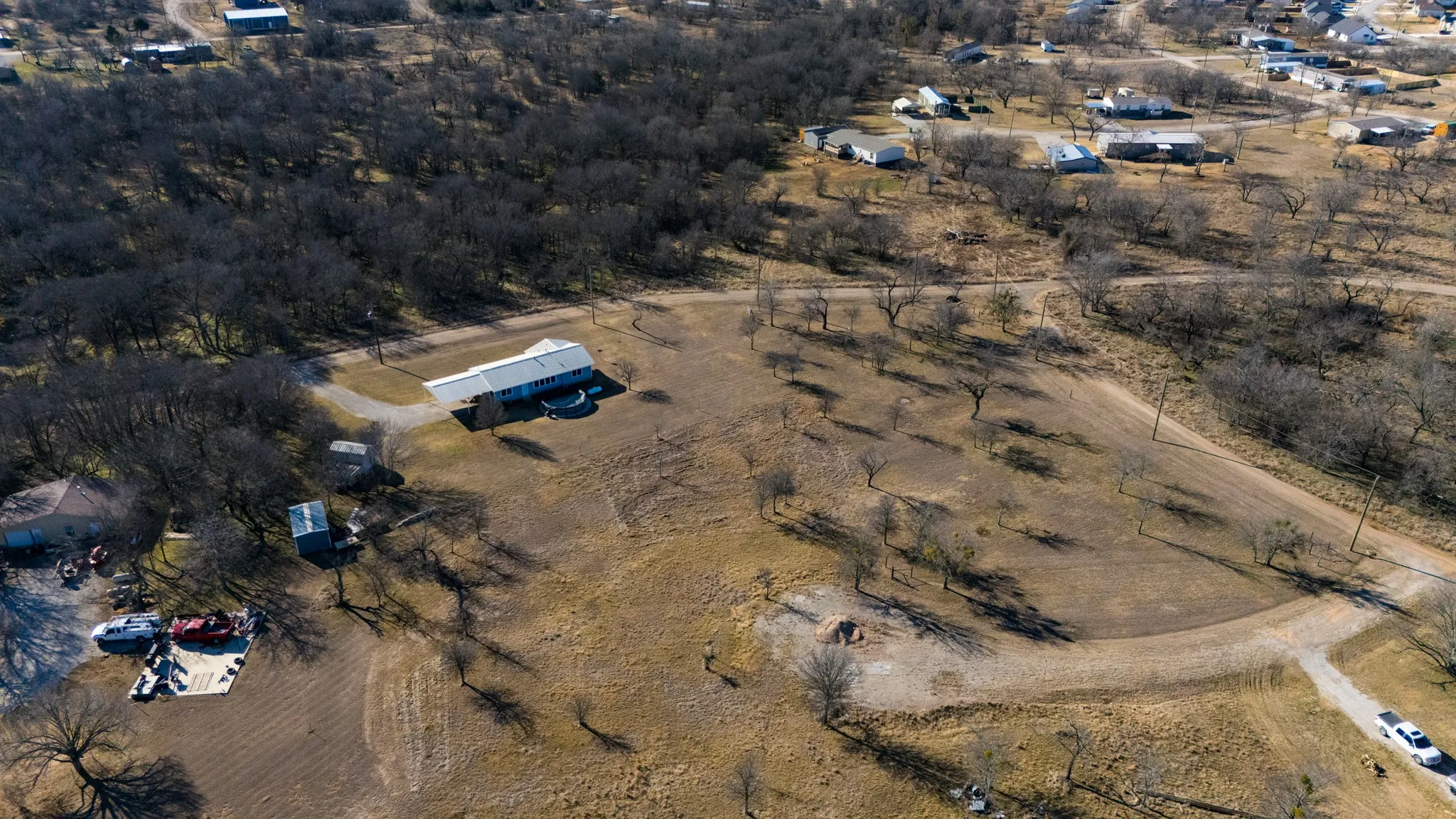 Expansive property with a single-story residence, multiple outbuildings, and mature trees situated on a large lot