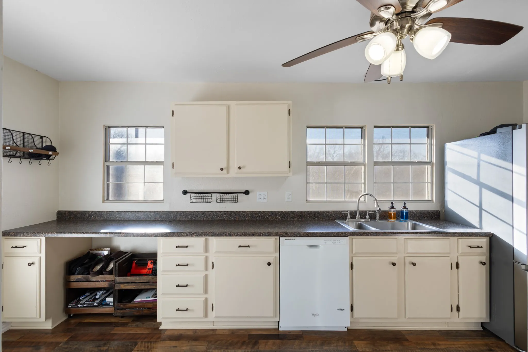 Kitchen featuring wood-finish flooring, cream cabinetry, speckled countertops, a stainless steel double basin sink with a gooseneck faucet, and multiple windows
