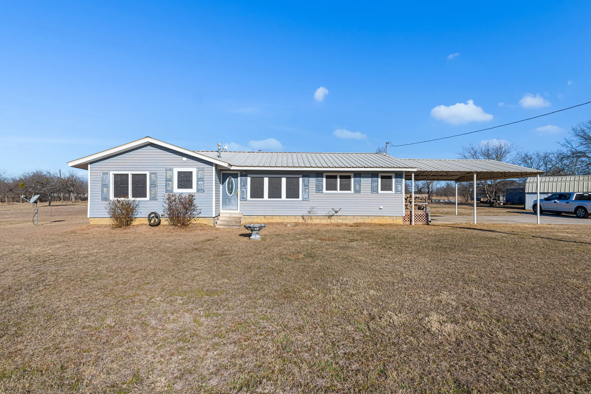 Light blue siding exterior with a metal roof, prominent covered carport, and a white entry door