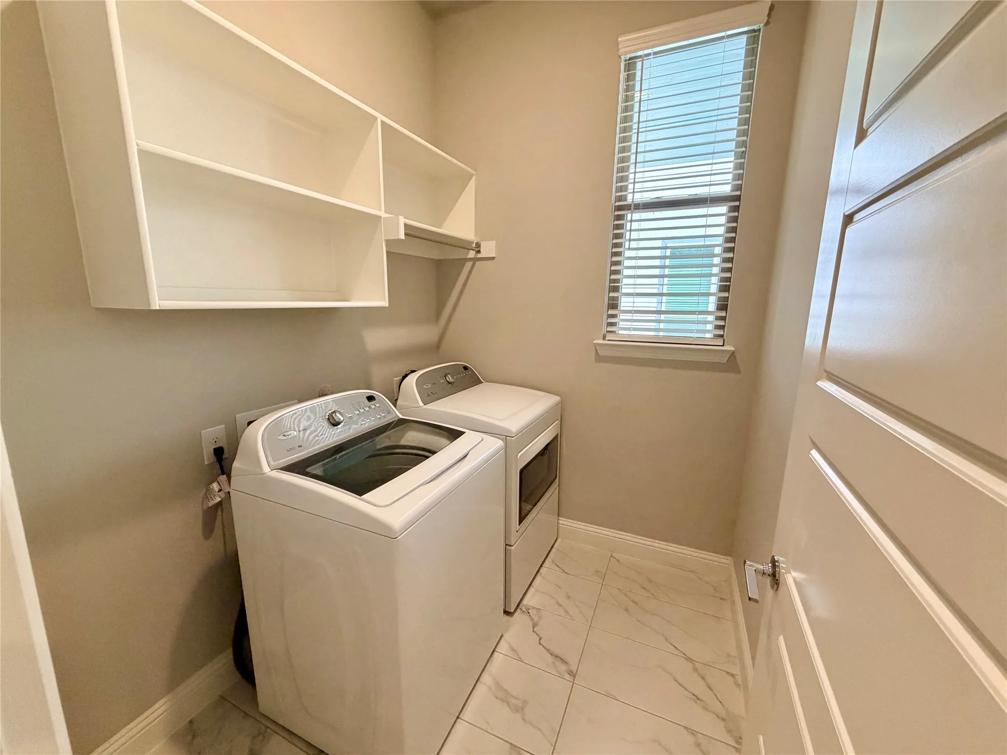 Laundry area featuring built-in shelving, a hanging rod, a window with blinds, and tile flooring