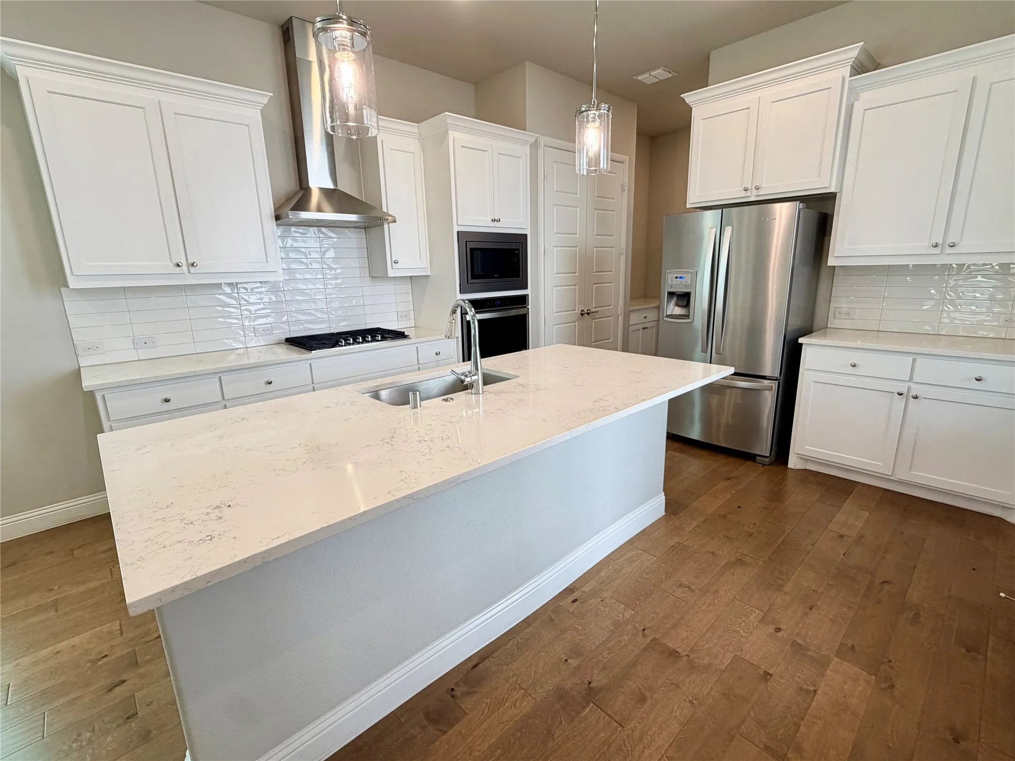 White cabinetry, stainless steel appliances, central island with sink, wood-finish flooring, and subway tile backsplash