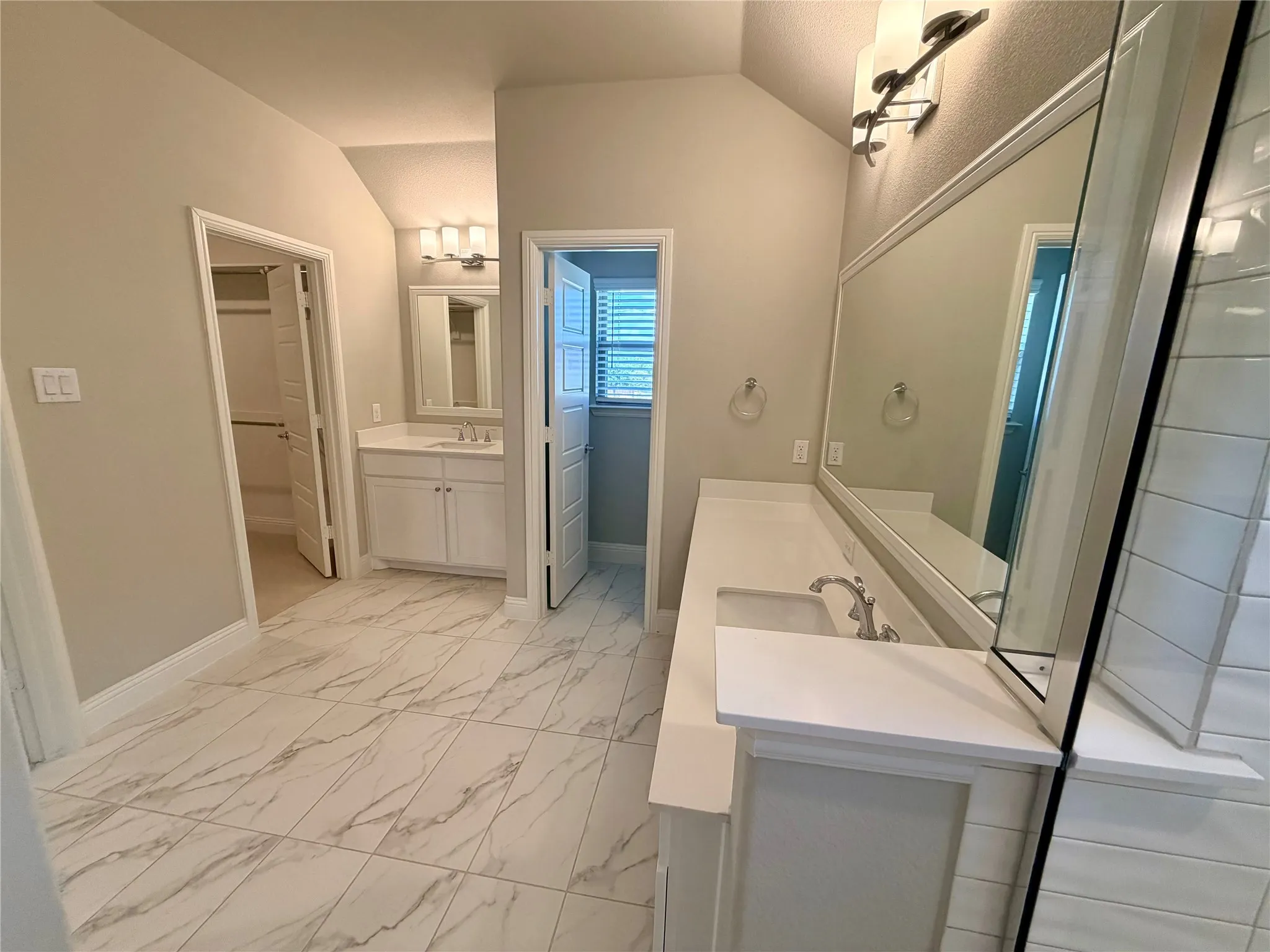 Dual vanity with integrated sinks, expansive mirror, contemporary light fixtures, white cabinetry, and large format tile flooring