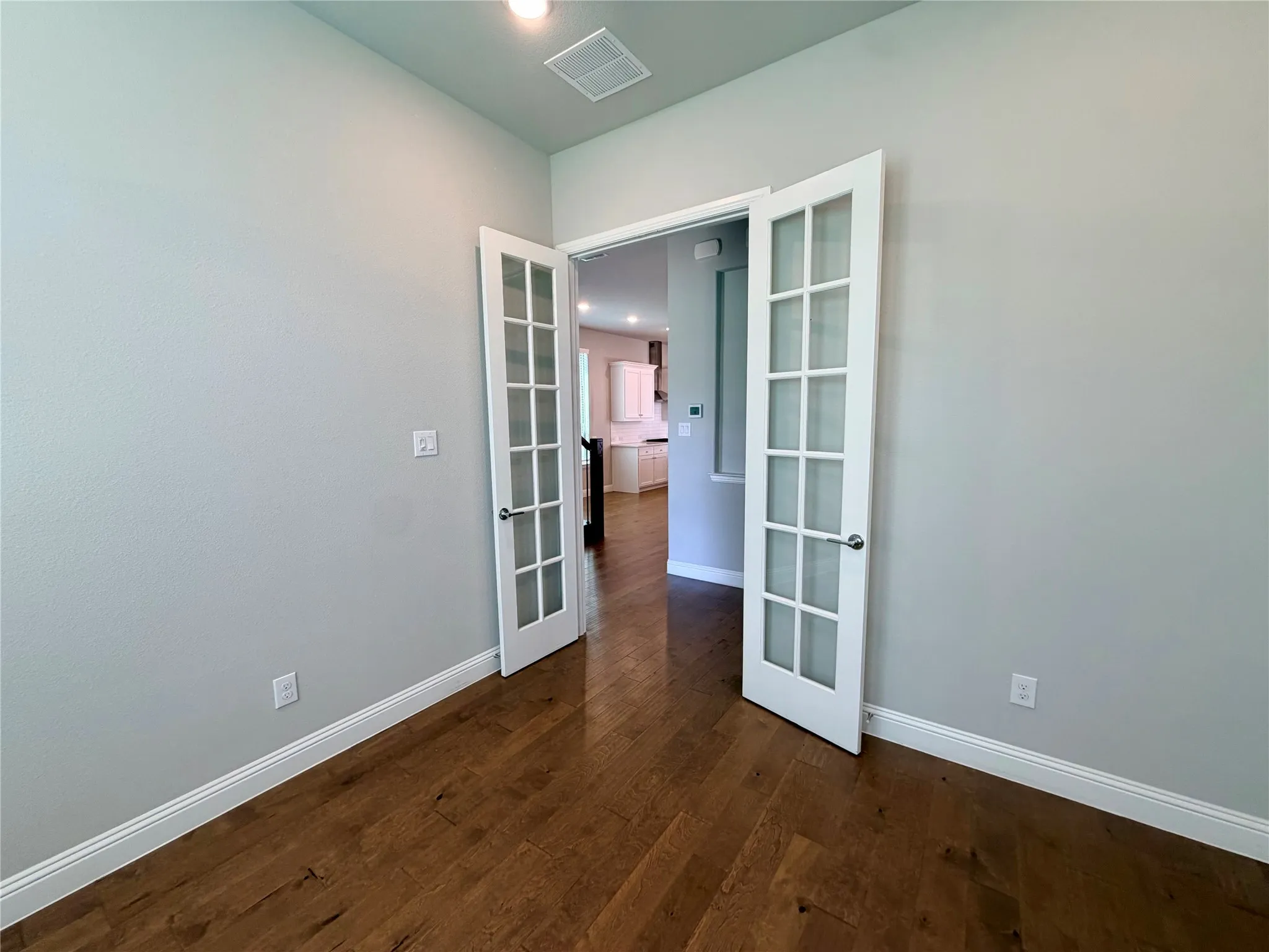 Room with wood-finish flooring, light neutral wall paint, and double French doors with frosted glass panels