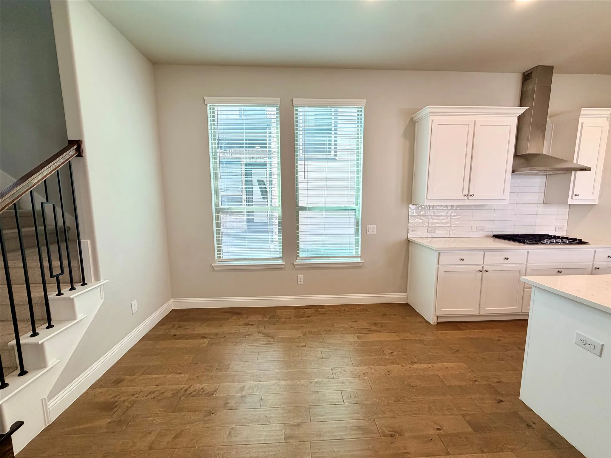 Wood-finish flooring, white kitchen cabinetry, subway tile backsplash, white countertops, and a modern range hood