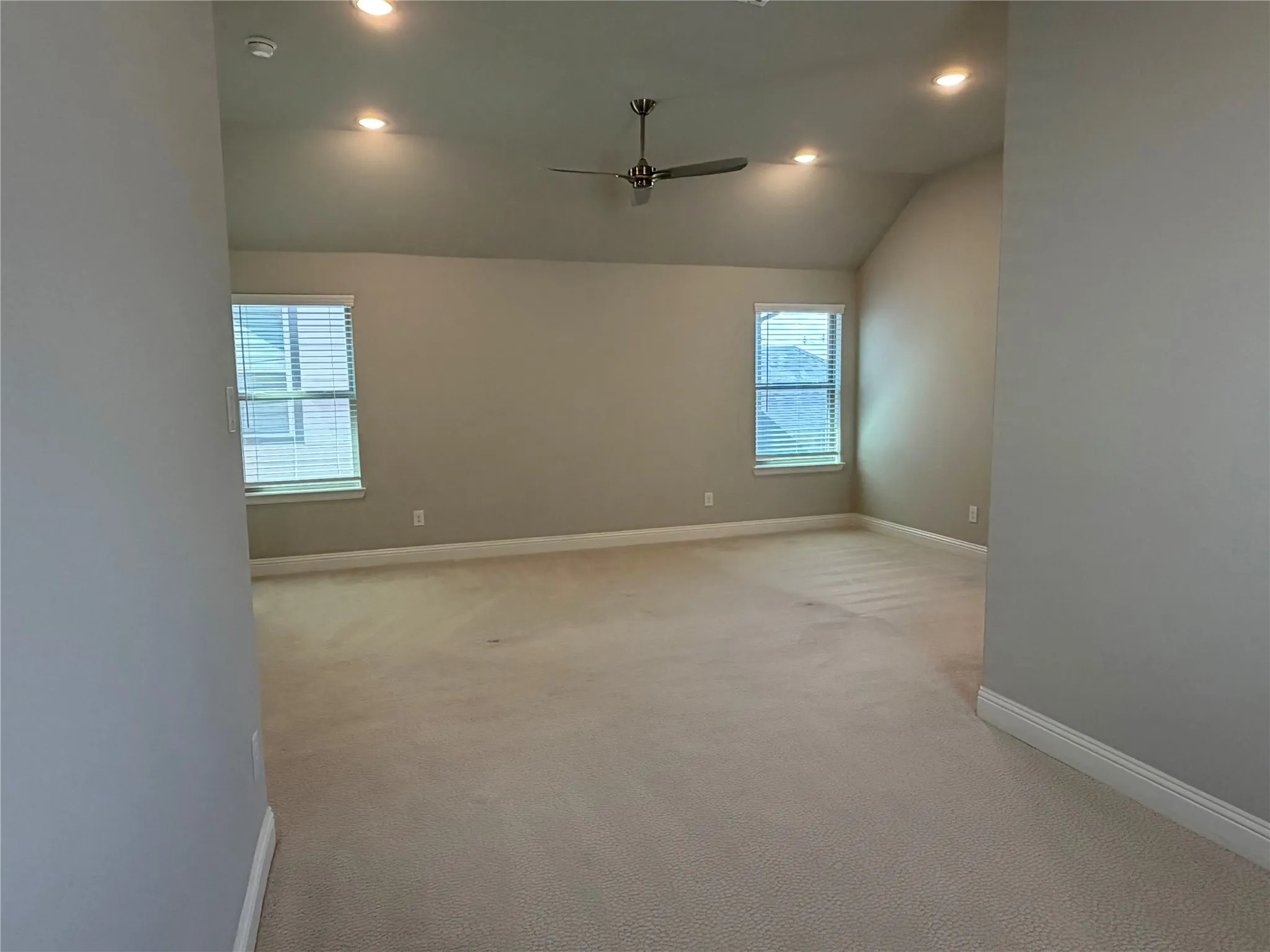 Vaulted ceiling with recessed lighting and ceiling fan, neutral carpet, and twin windows with blinds