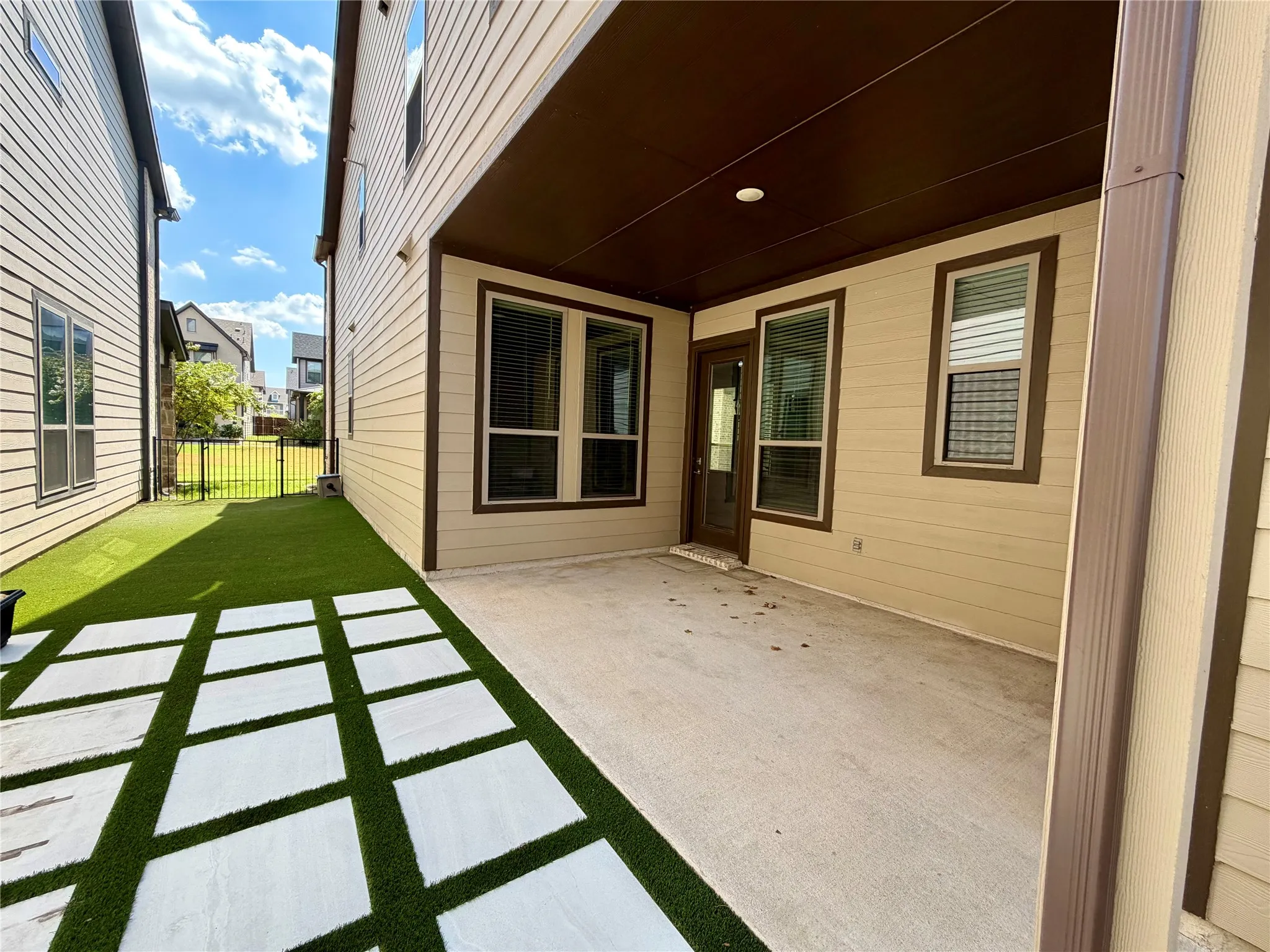 Covered concrete patio with recessed lighting, artificial turf, and square paver stepping stones