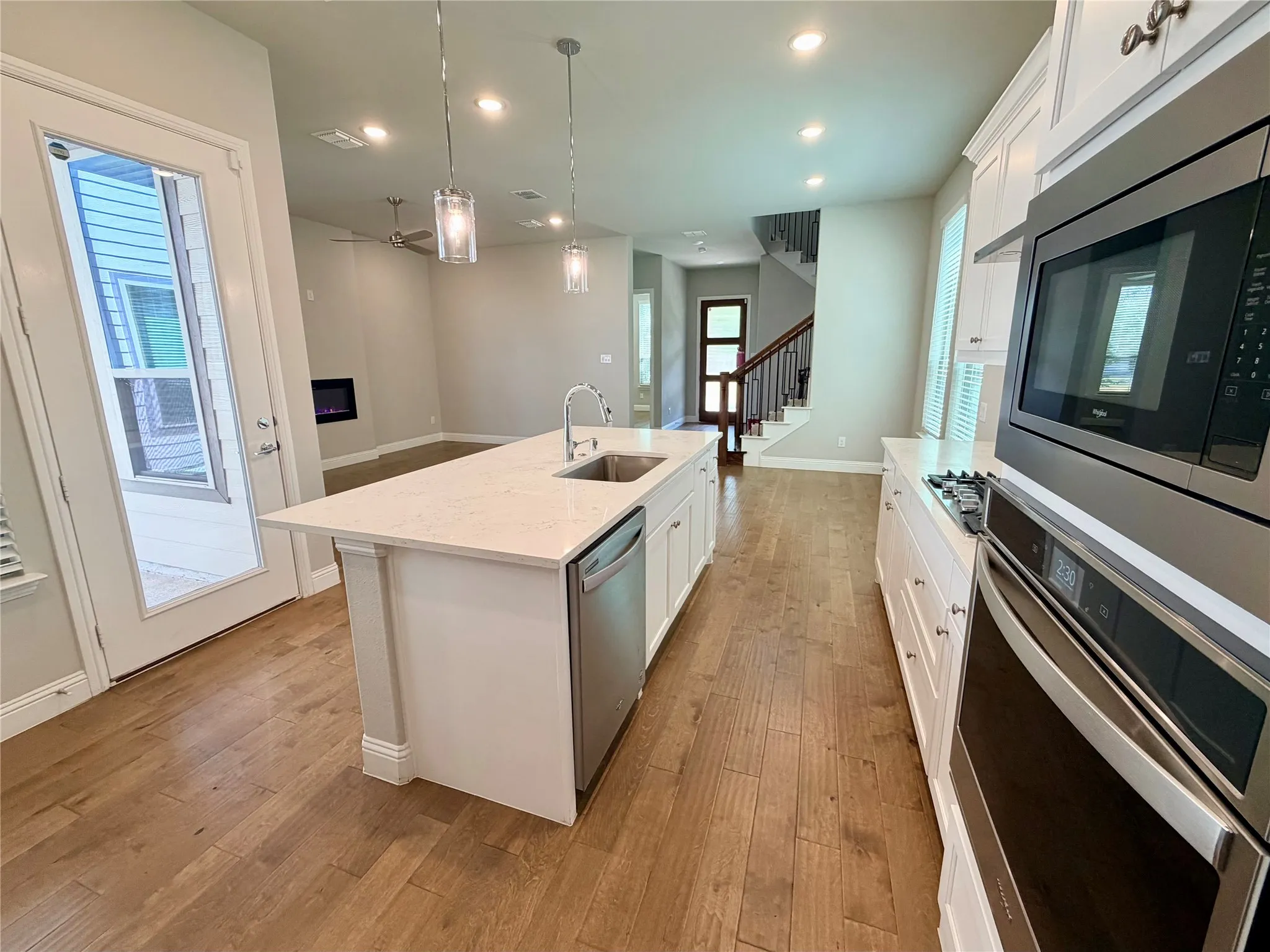 Kitchen featuring an island with sink, stainless steel appliances, wood-finish flooring, and white cabinetry