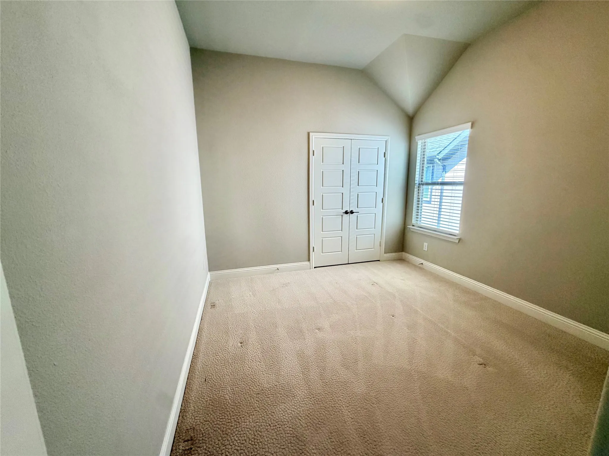 Vaulted ceiling, neutral wall paint, carpeted flooring, window with blinds, paneled double doors