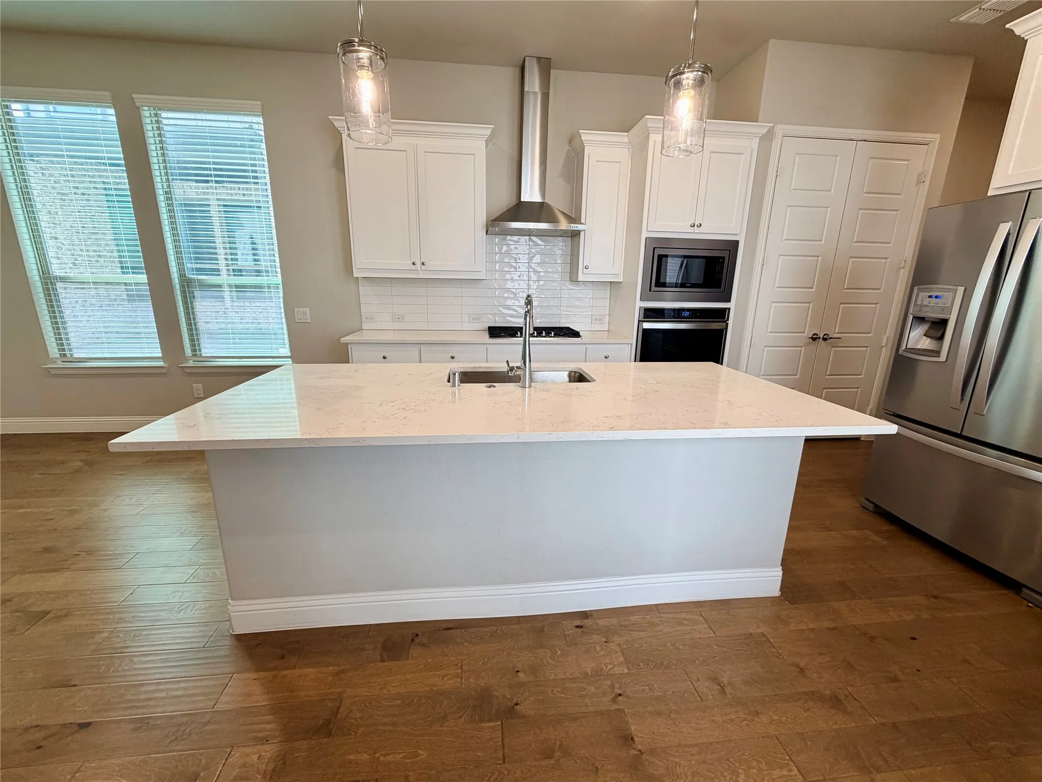 Kitchen featuring an island with a built-in sink, stainless steel appliances, white cabinetry, tile backsplash, and wood-finish flooring