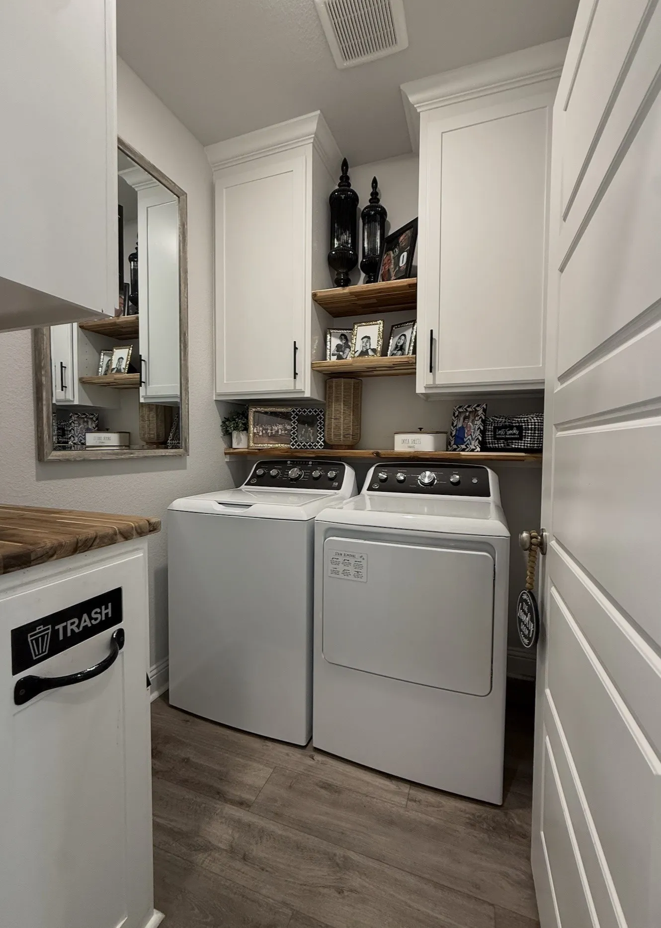 White shaker-style cabinetry with crown molding, wood-finish flooring, and floating wood shelves