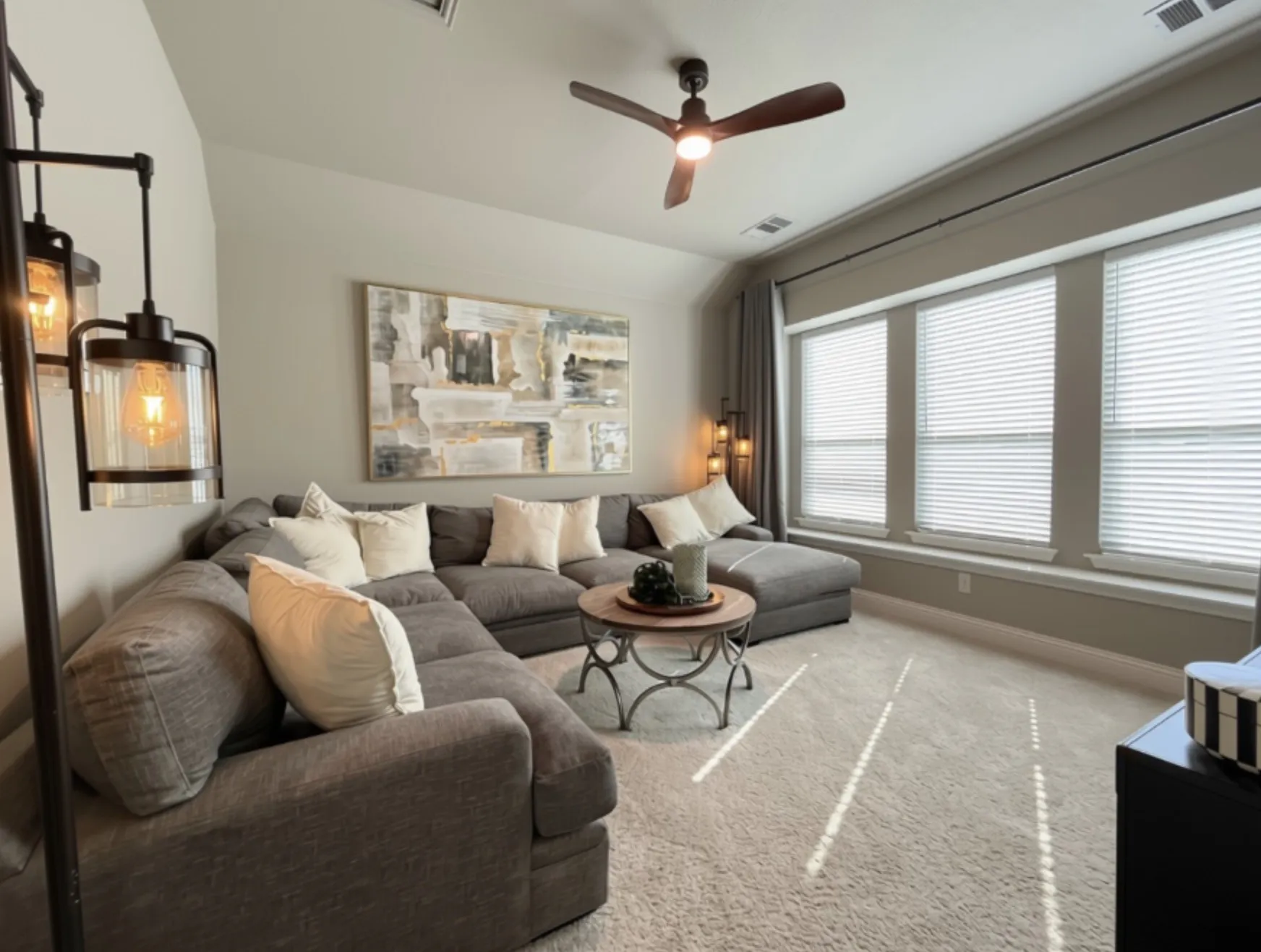 Bright living area featuring a ceiling fan, three large windows with blinds, and light-colored carpeting
