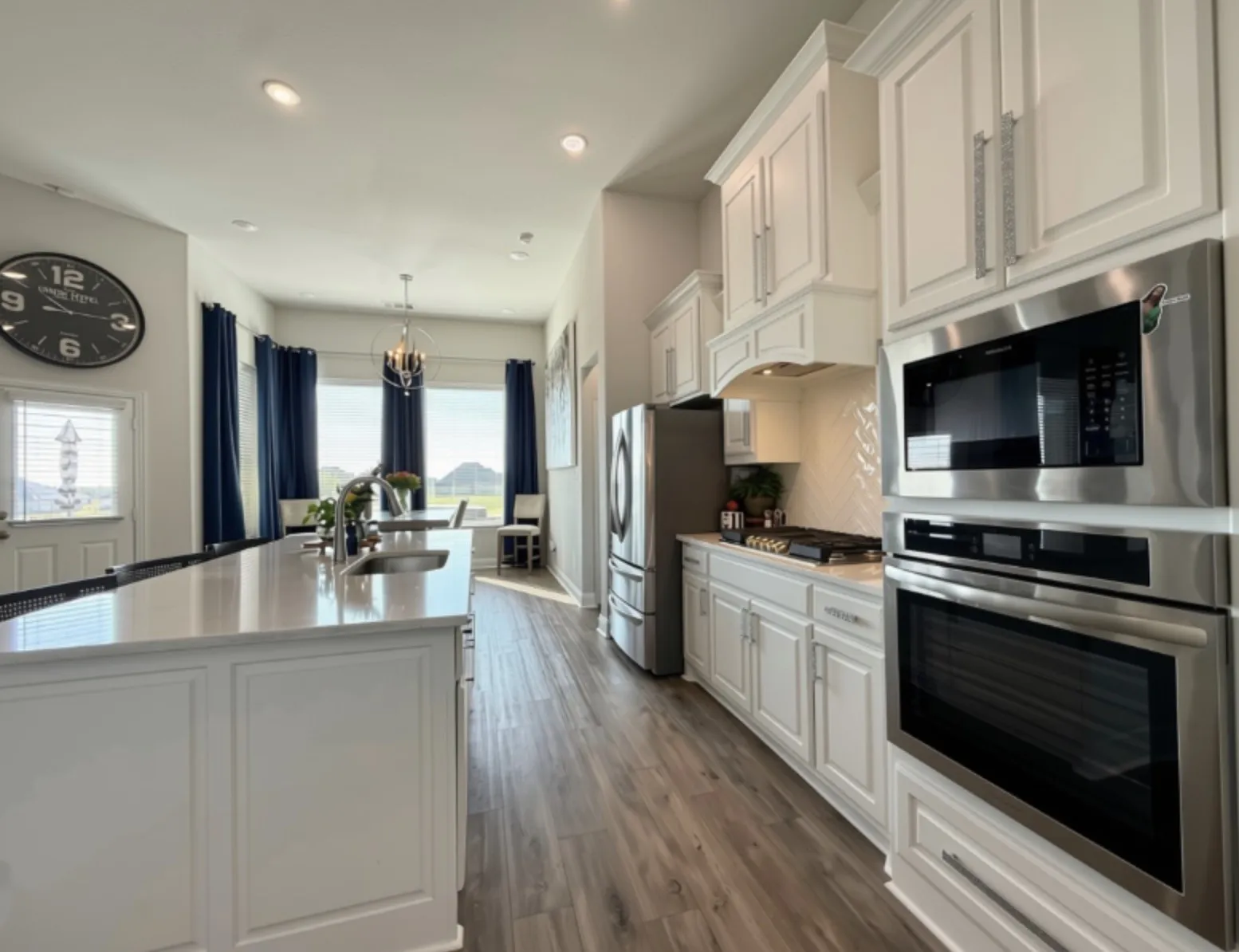 Kitchen featuring white cabinetry, stainless steel appliances, a center island with sink, wood-finish flooring, and recessed lighting