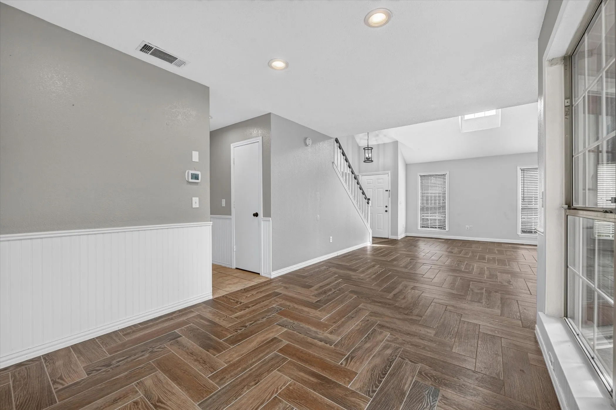 Dining room and living room from far corner of dining room. Has wainscoting and recessed lighting.