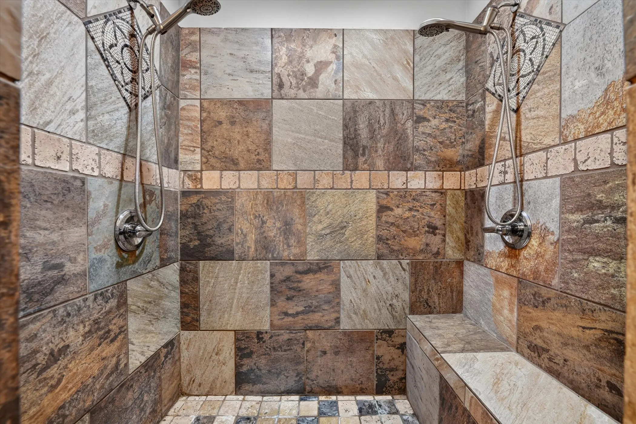 Primary shower with decorative mosaic inlays, dual shower heads, and built-in bench.