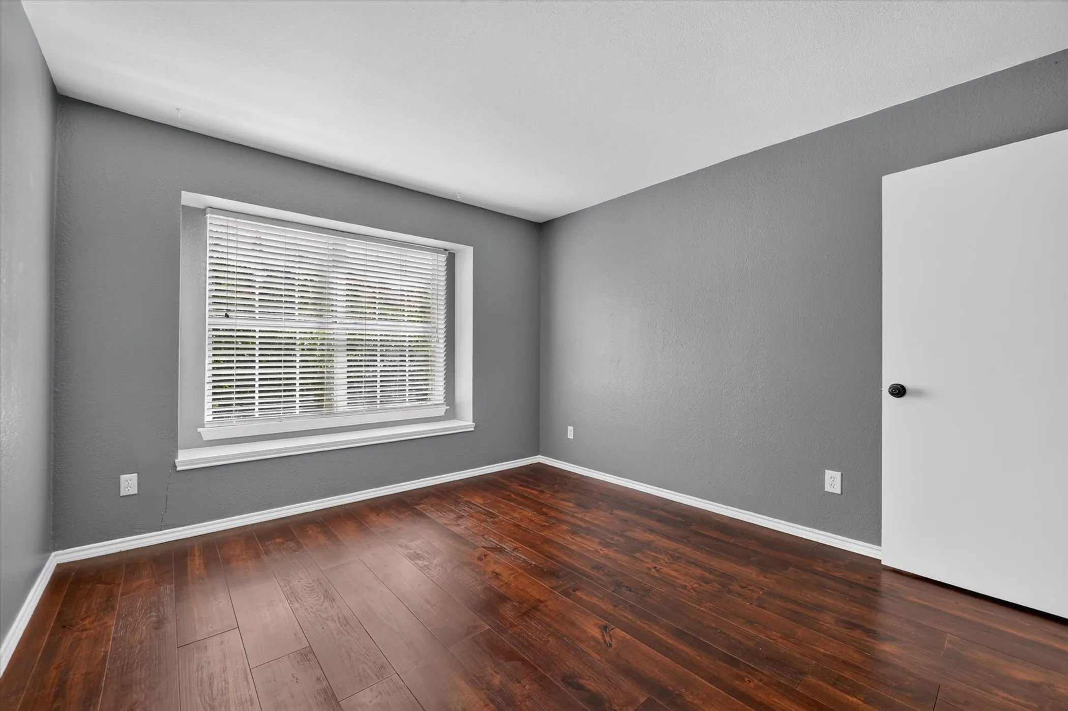 Wood-finish flooring, neutral gray wall tones, and a window with white blinds