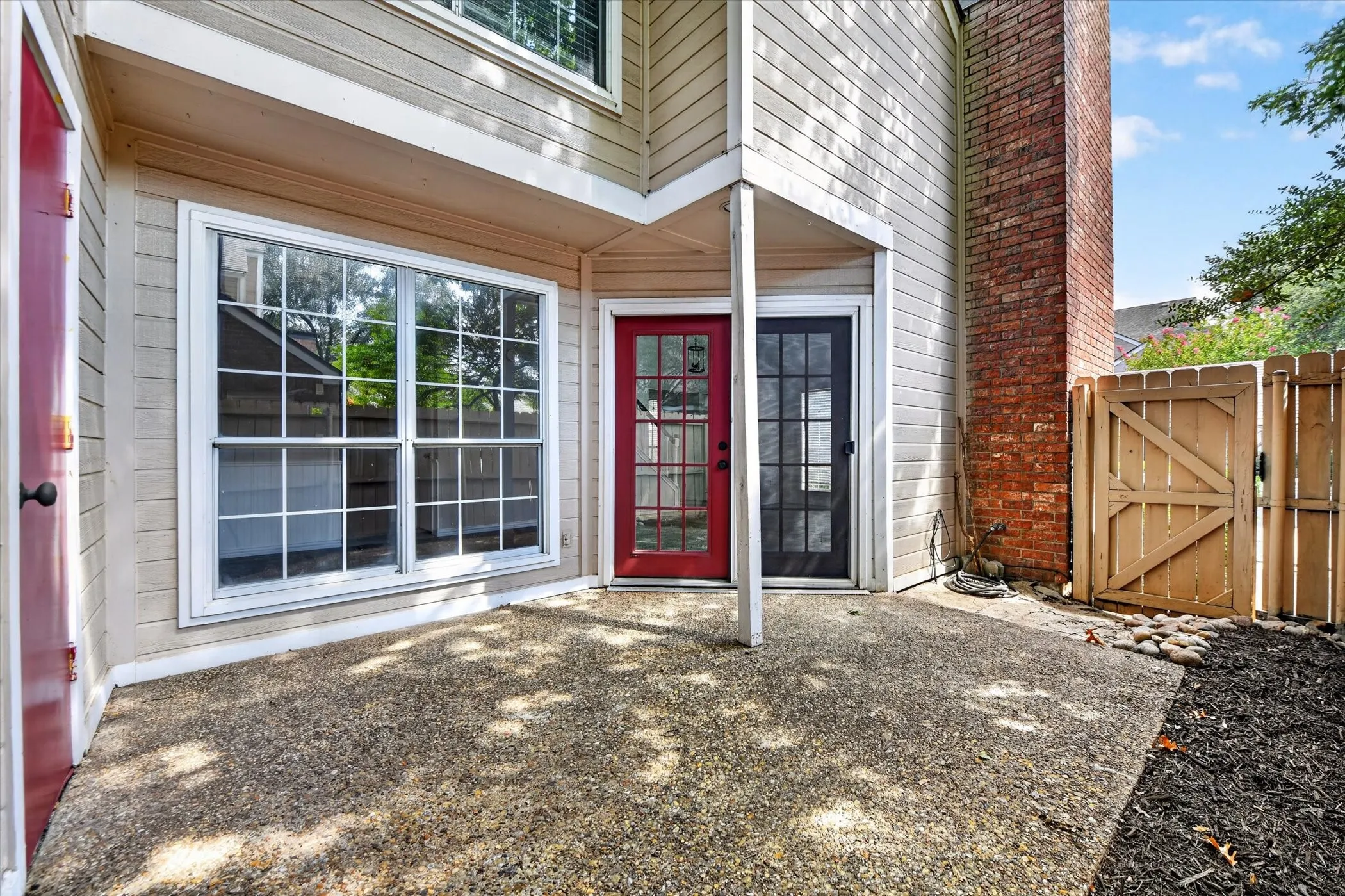Concrete patio with a red paneled door, a black paneled door, and a large multi-pane window